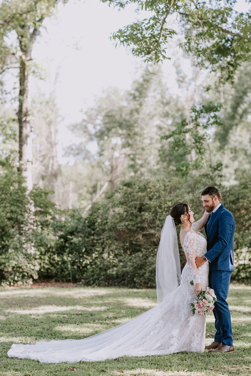 Wedding couple embraces in romantic outdoor garden setting with flowing lace veil.