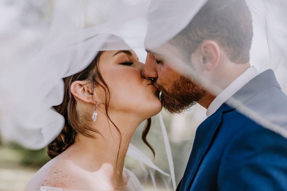Intimate kiss captured between couple under flowing white veil.