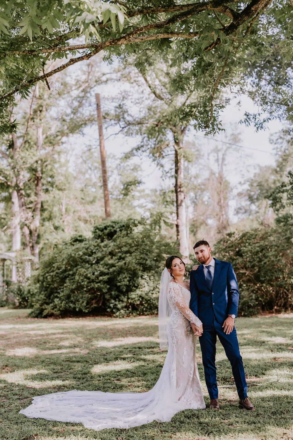 Couple poses together in wooded garden setting wearing formal wedding attire.