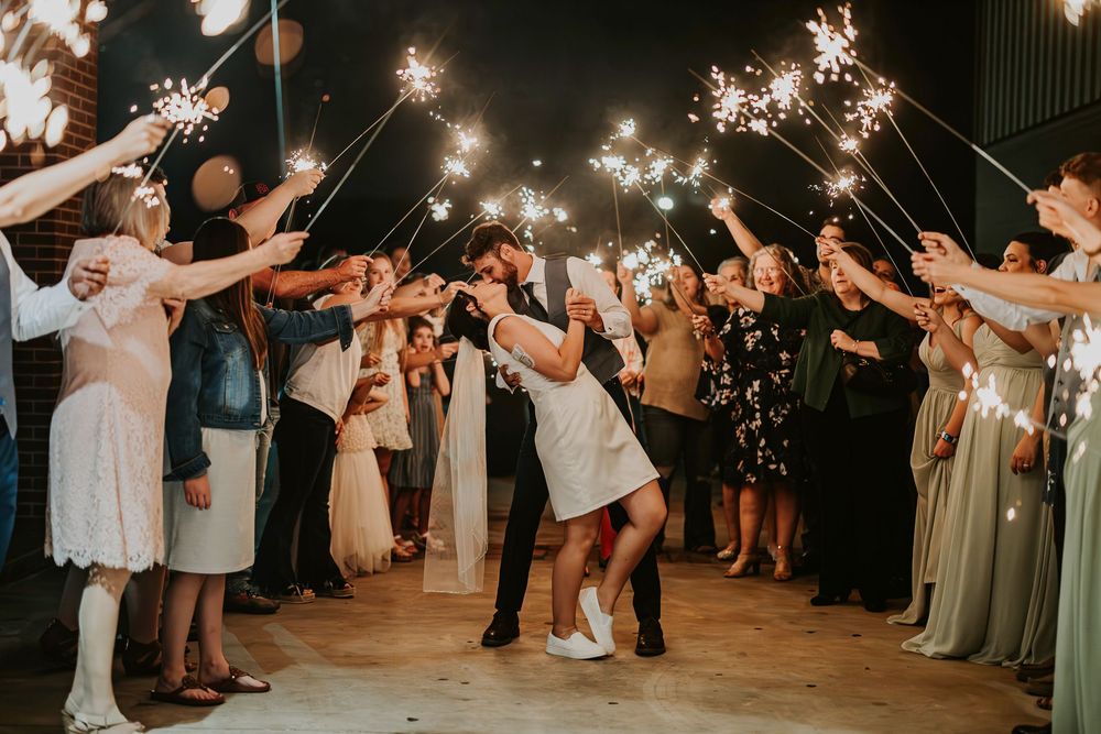 Wedding guests hold sparklers in a nighttime celebration forming a magical tunnel of light.