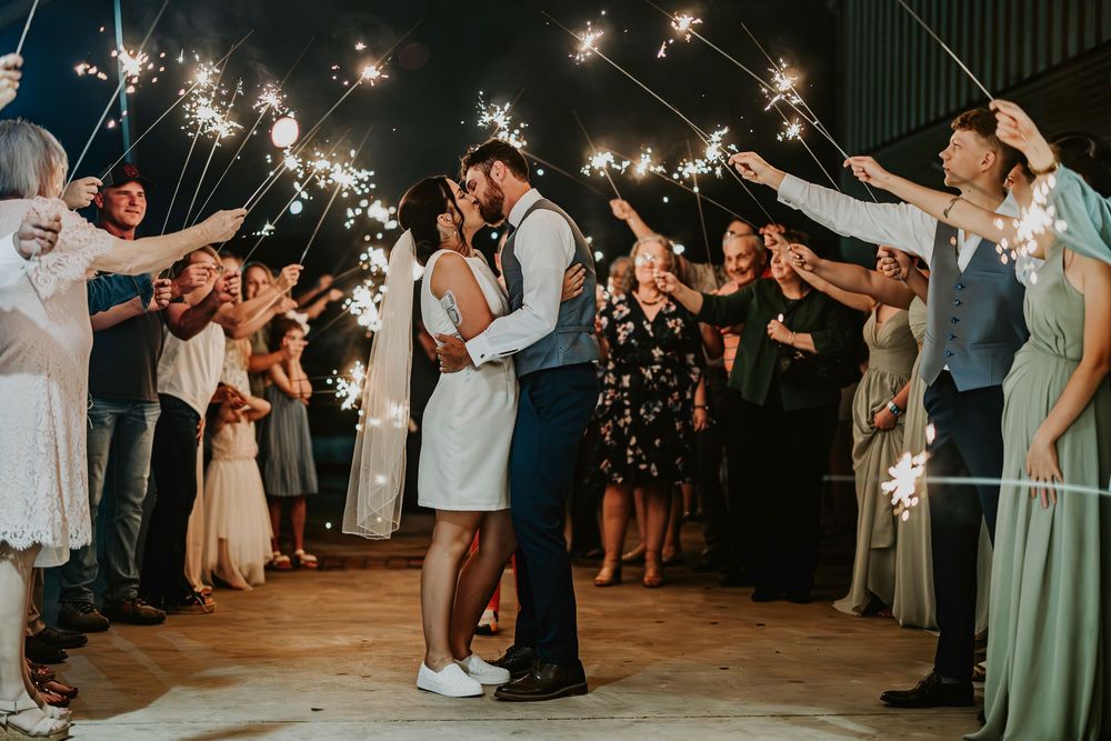Wedding party celebrates with sparklers creating a glowing archway at night.