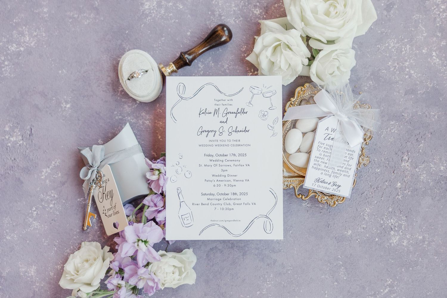 Elegant white wedding invitations with roses and gold accents arranged on textured gray background.