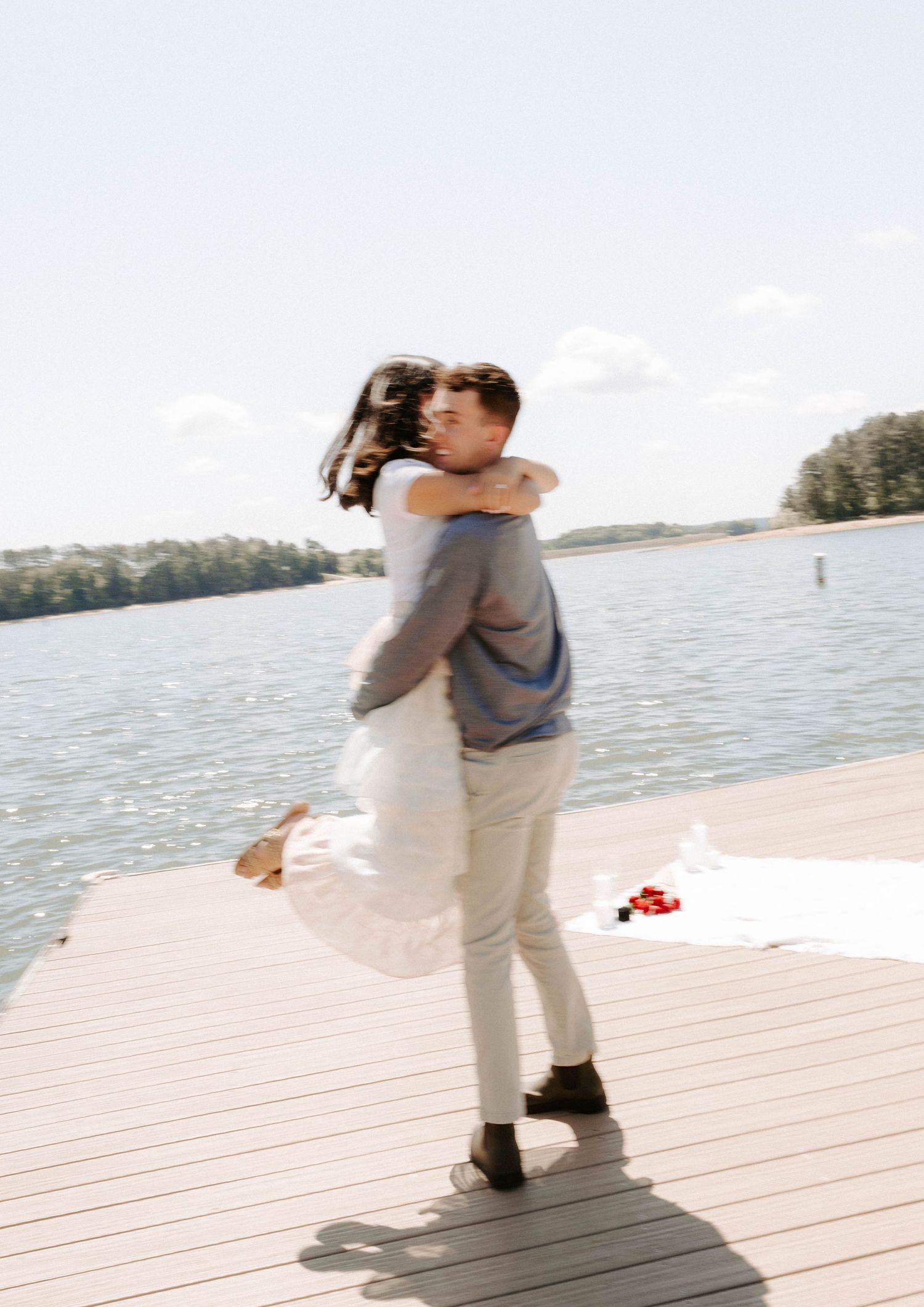A couple embraces outdoors in casual attire, with the person in white sweater and person in light denim sharing tender moments.