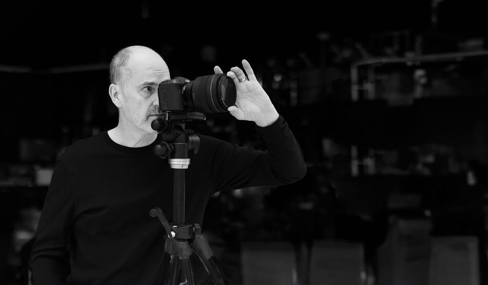 Black and white portrait of professional photographer with an engineering background holding camera equipment.