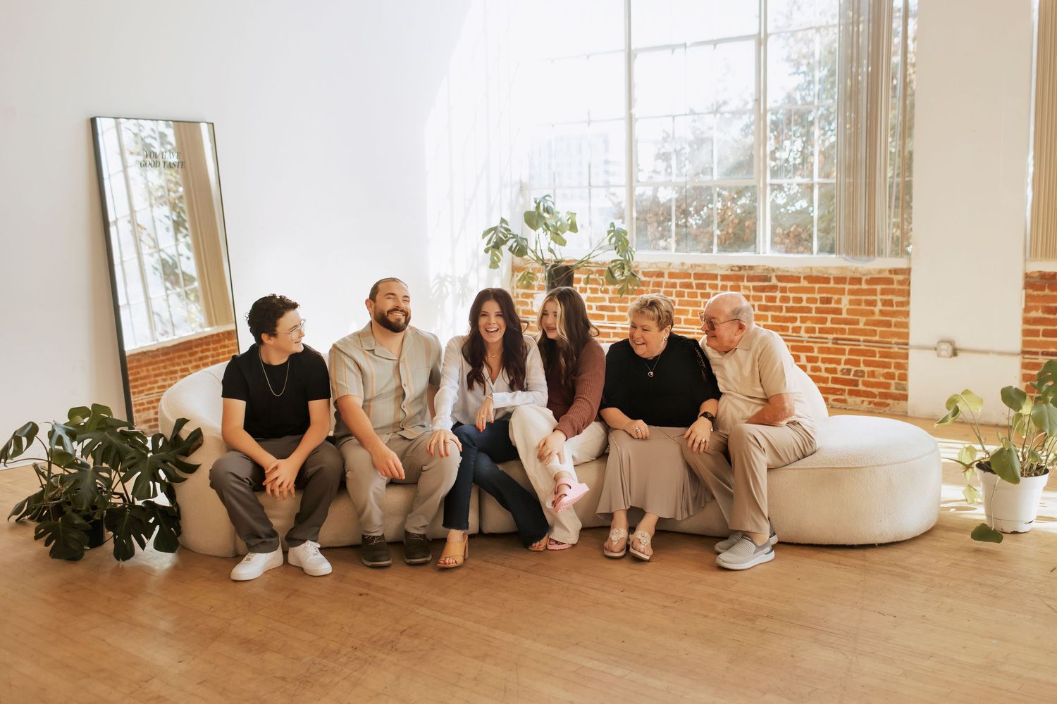 An extended family laughs and smiles together on a couch in a light and bright photography studio.