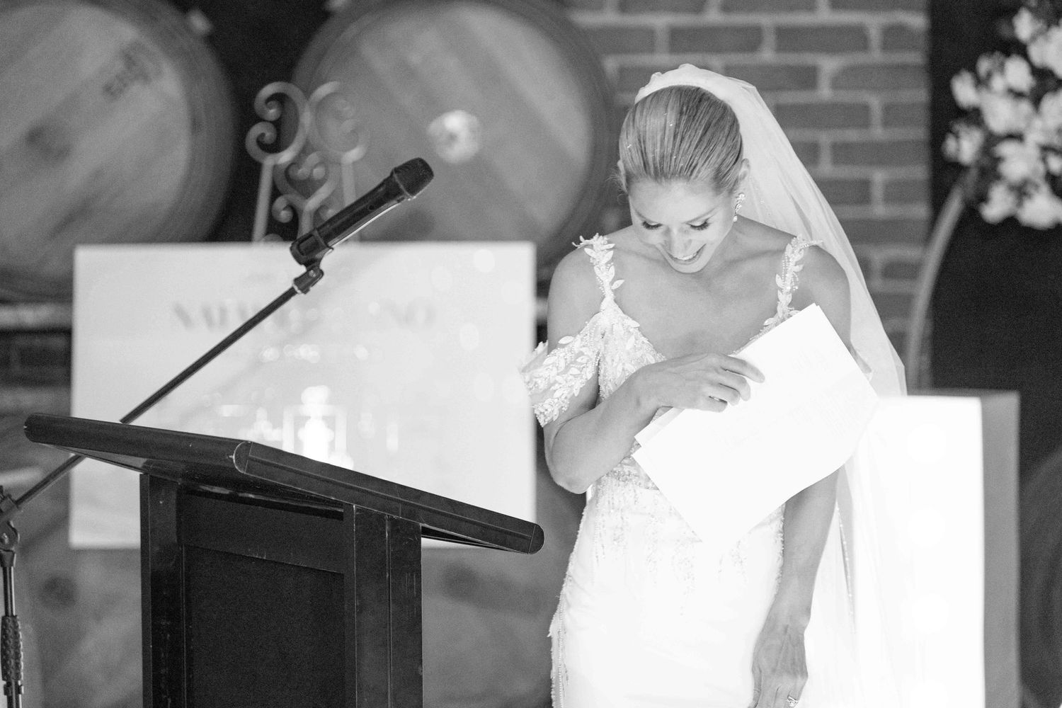 Emotional bride in wedding gown bowing at podium during wedding reception speech, black and white.