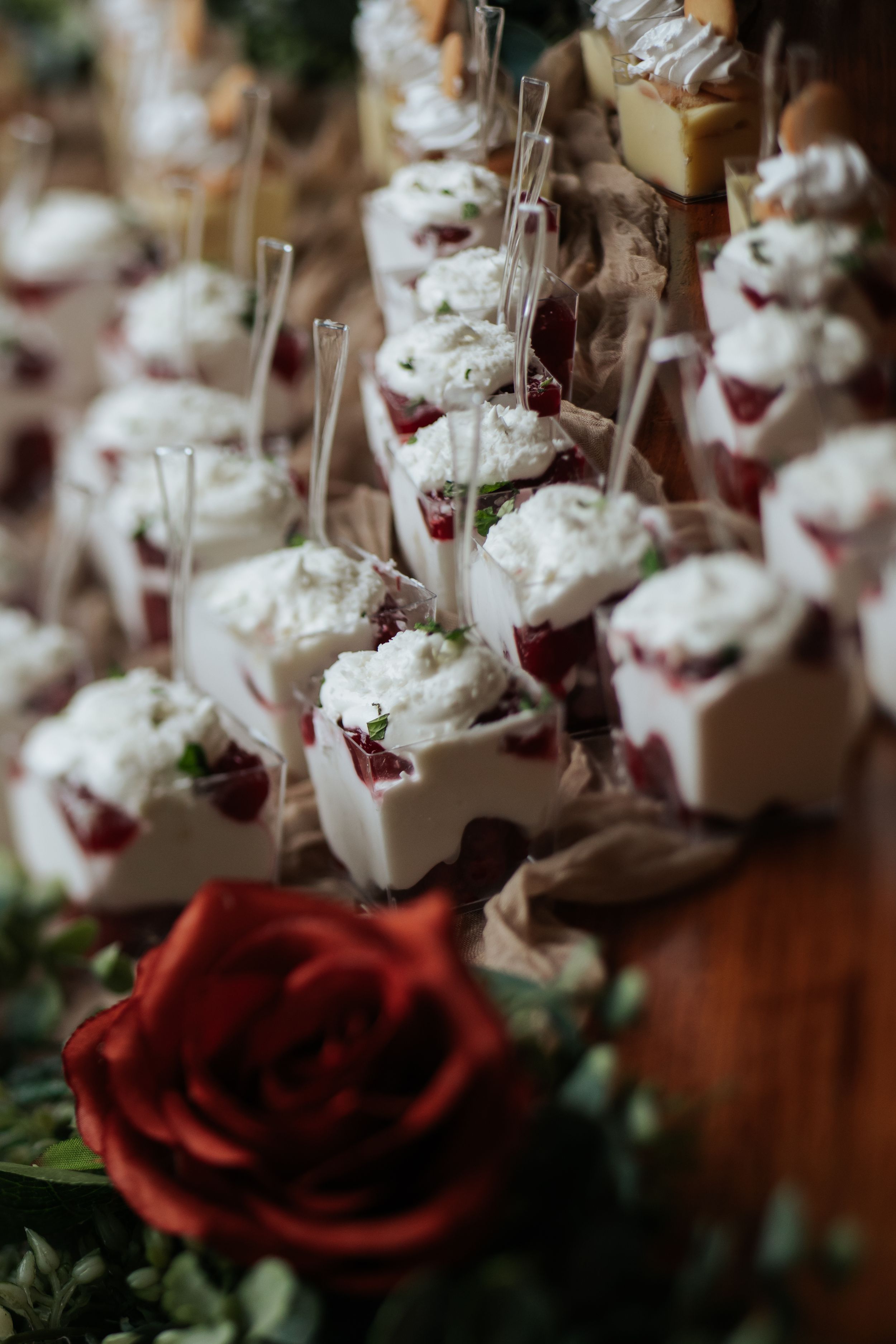 Wedding dessert display with mini cream parfaits garnished with red berries and roses.