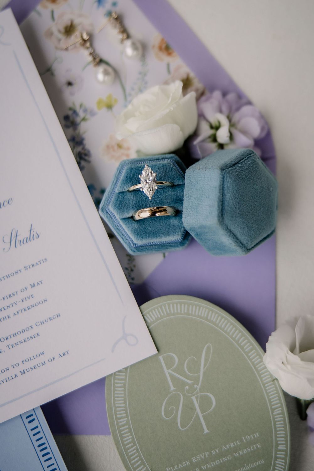 Wedding invitation details with teal velvet ring box and white flowers on purple and sage green styling surfaces.