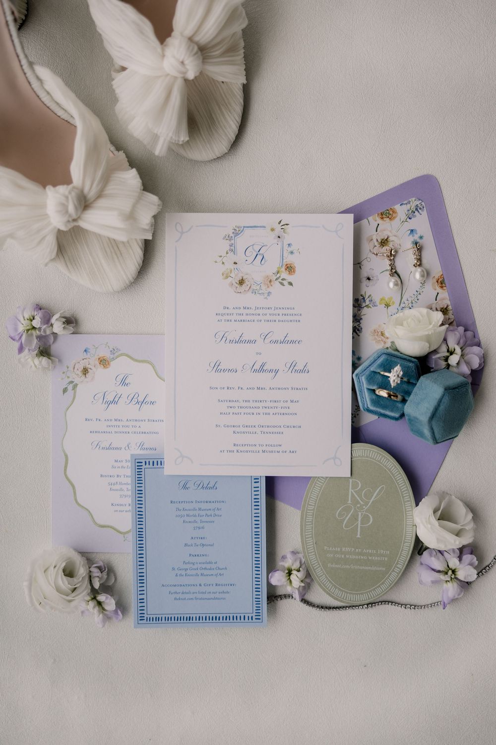 Elegant wedding invitation suite in white, blue and lilac colors with floral designs laid out on a light surface.