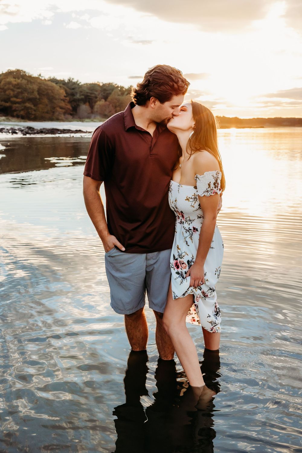 A couple shares a romantic moment while standing in shallow water at sunset by the beach.