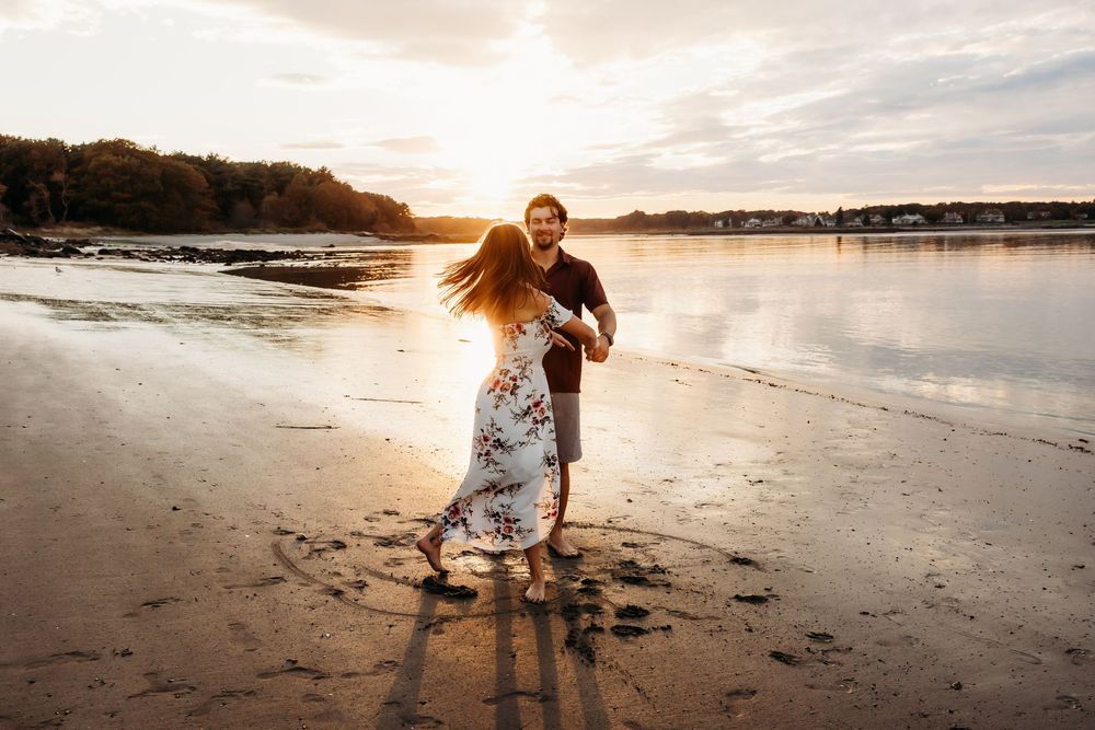 Two people dancing together on a beach at sunset with golden light streaming behind them on the shoreline.