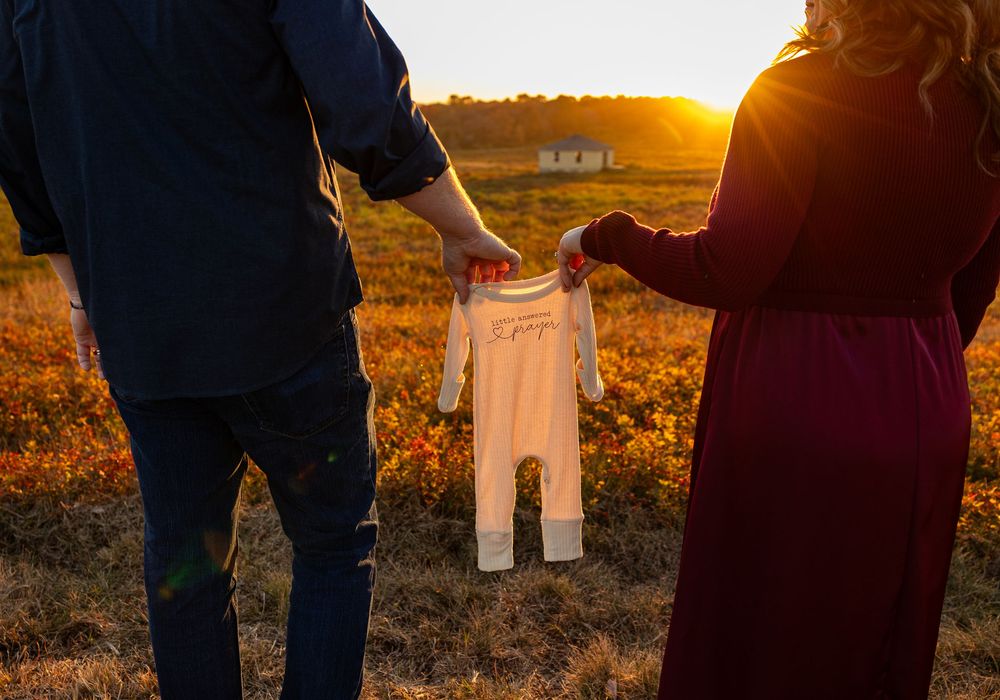 Silhouetted couple holding hands at sunset in a golden field with warm lighting.
