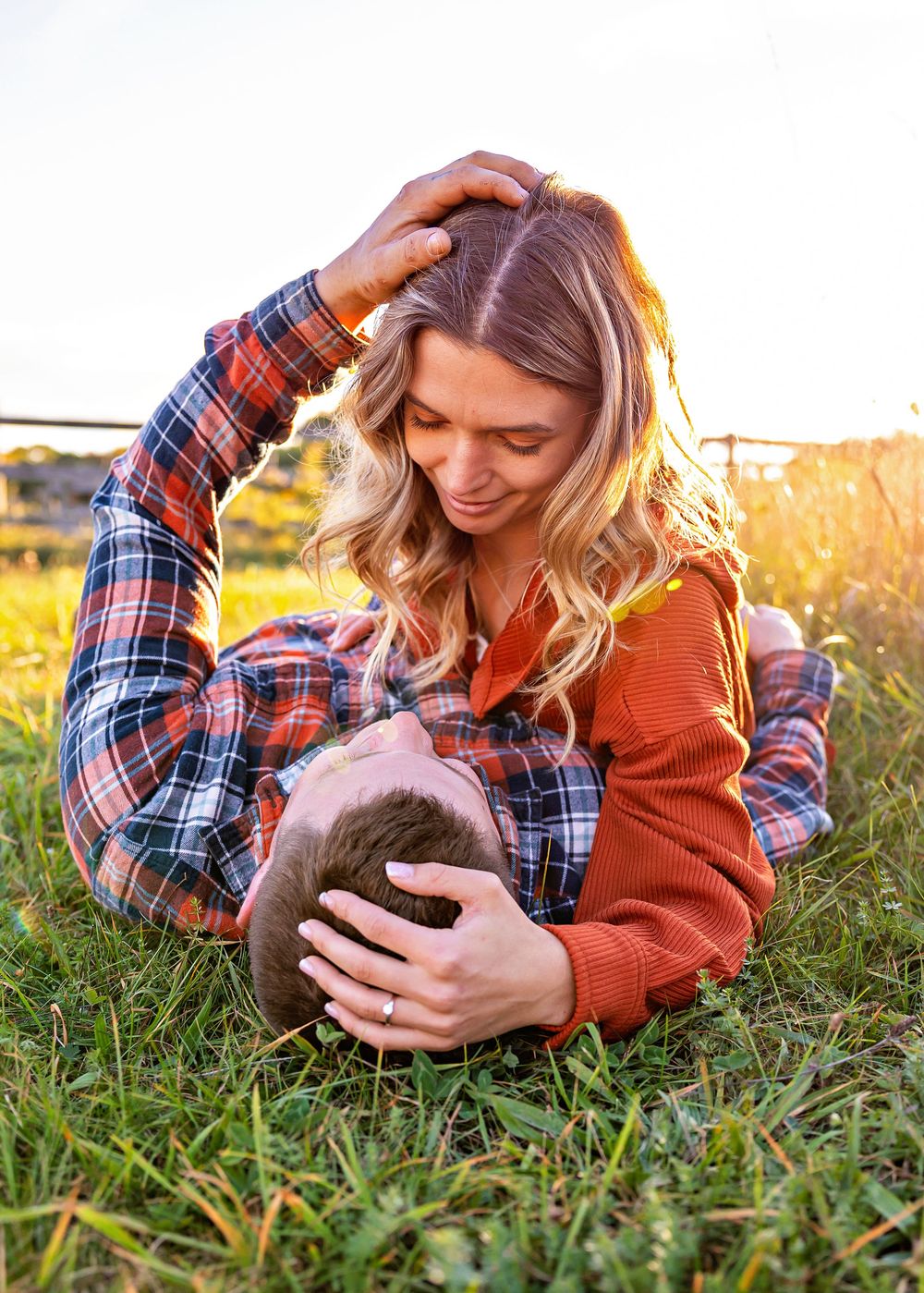 Someone in plaid and orange lying in grass holding a black cat during golden hour sunset.