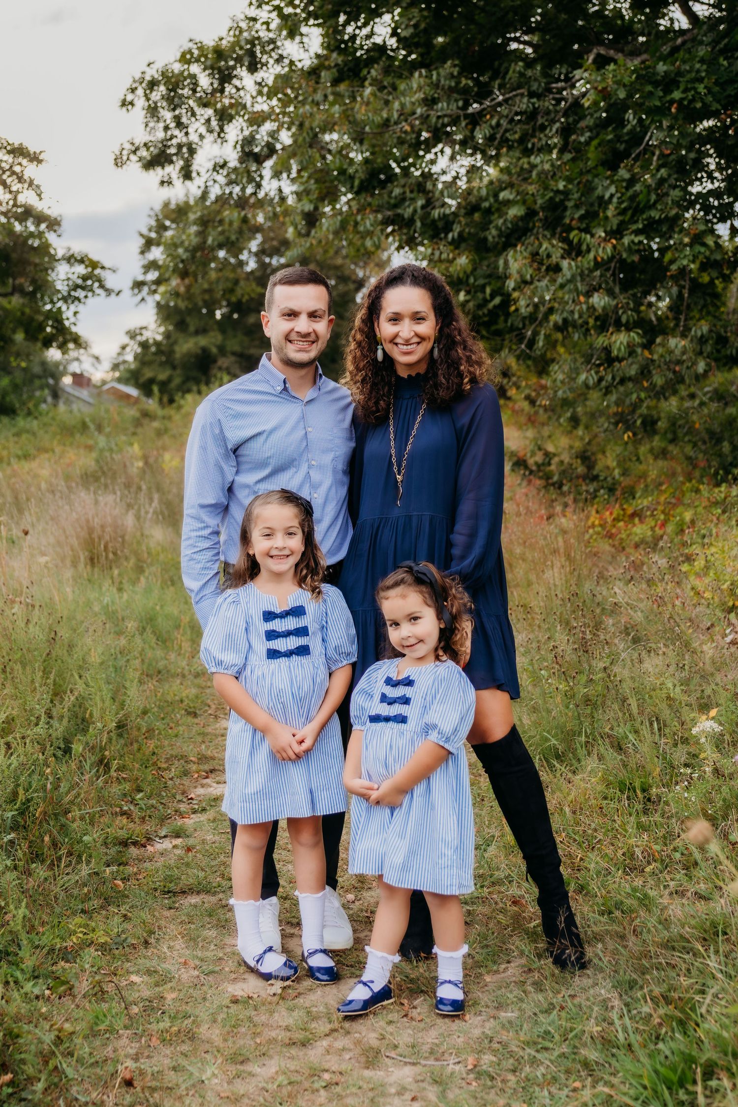A family in coordinated blue and black outfits poses together in a natural outdoor setting during autumn.