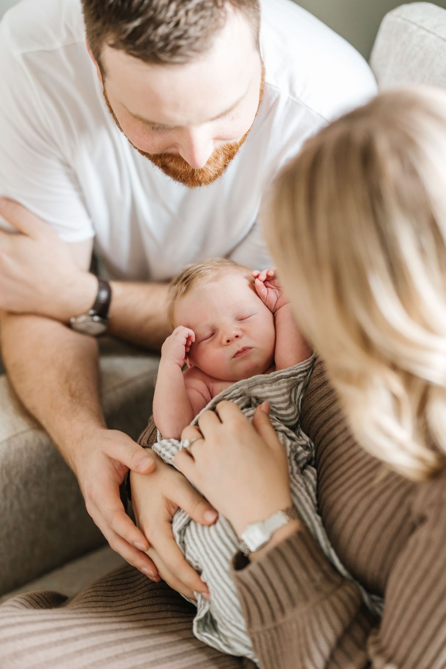 Parents tenderly watching their sleeping newborn baby while sitting together on a couch.