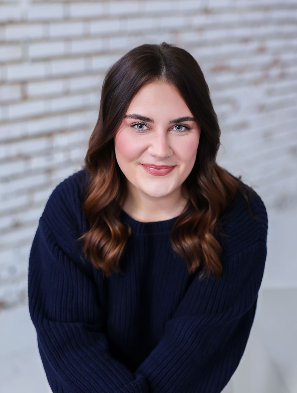 Professional headshots against a brick wall background showing warm expressions in a navy sweater.