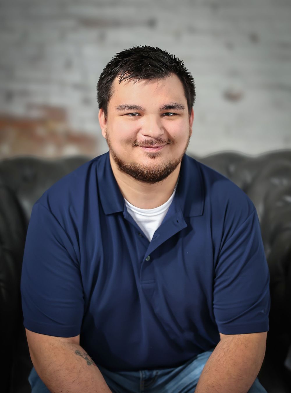 Professional headshot of person in navy polo against textured wall.