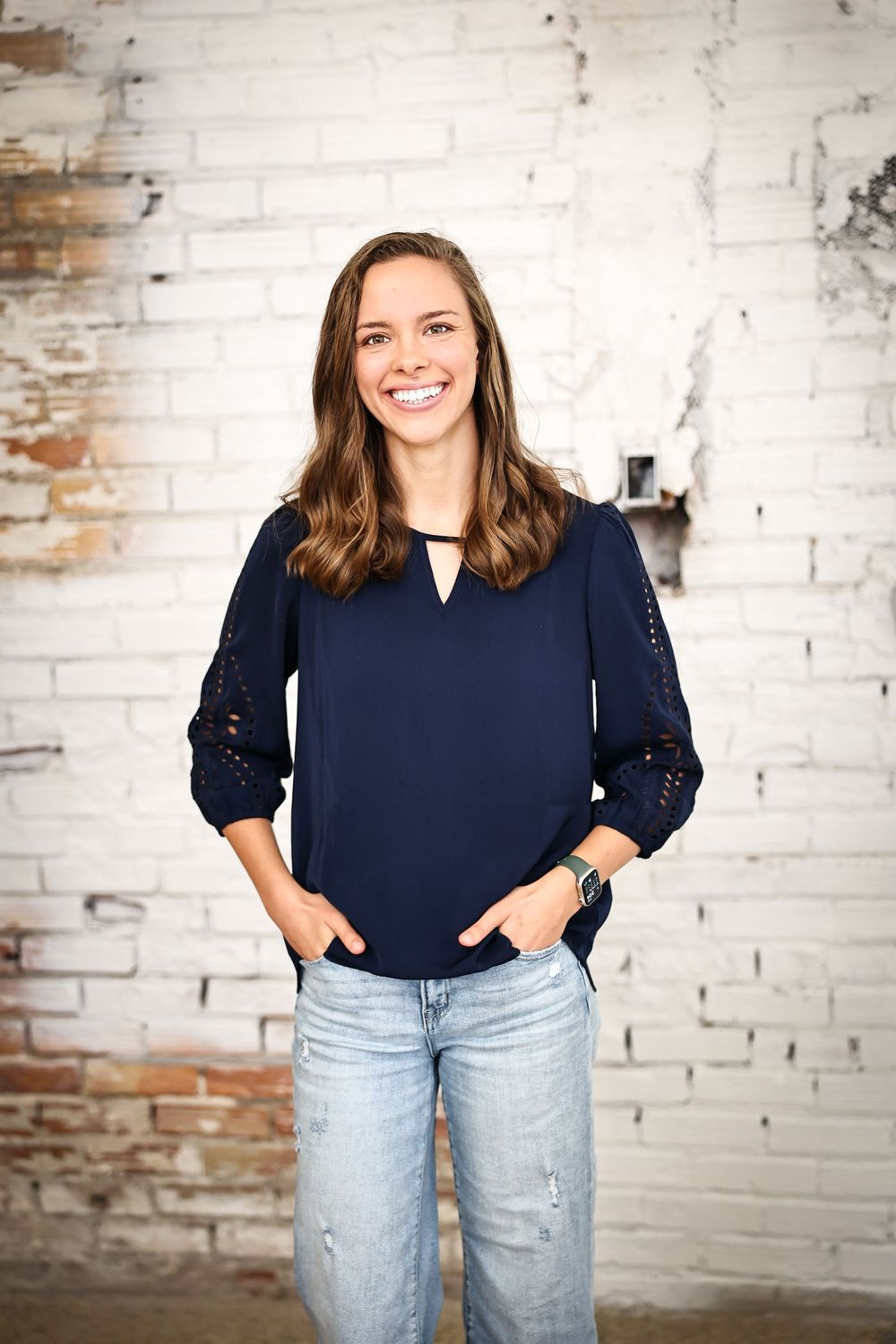 Casual portrait session against white brick wall wearing navy top and light jeans.