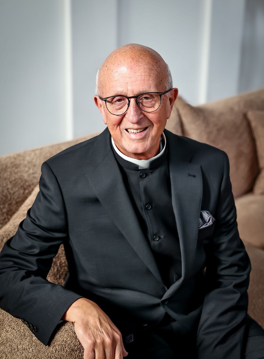 Professional portraits of someone in formal black attire seated on brown furniture.