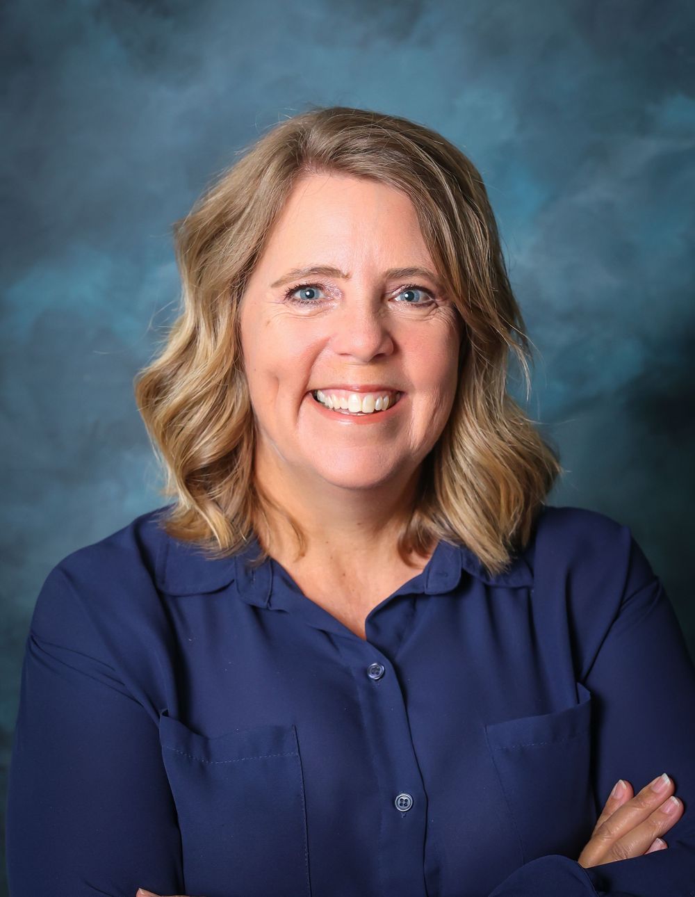 Professional portrait in navy blue top against blue backdrop.
