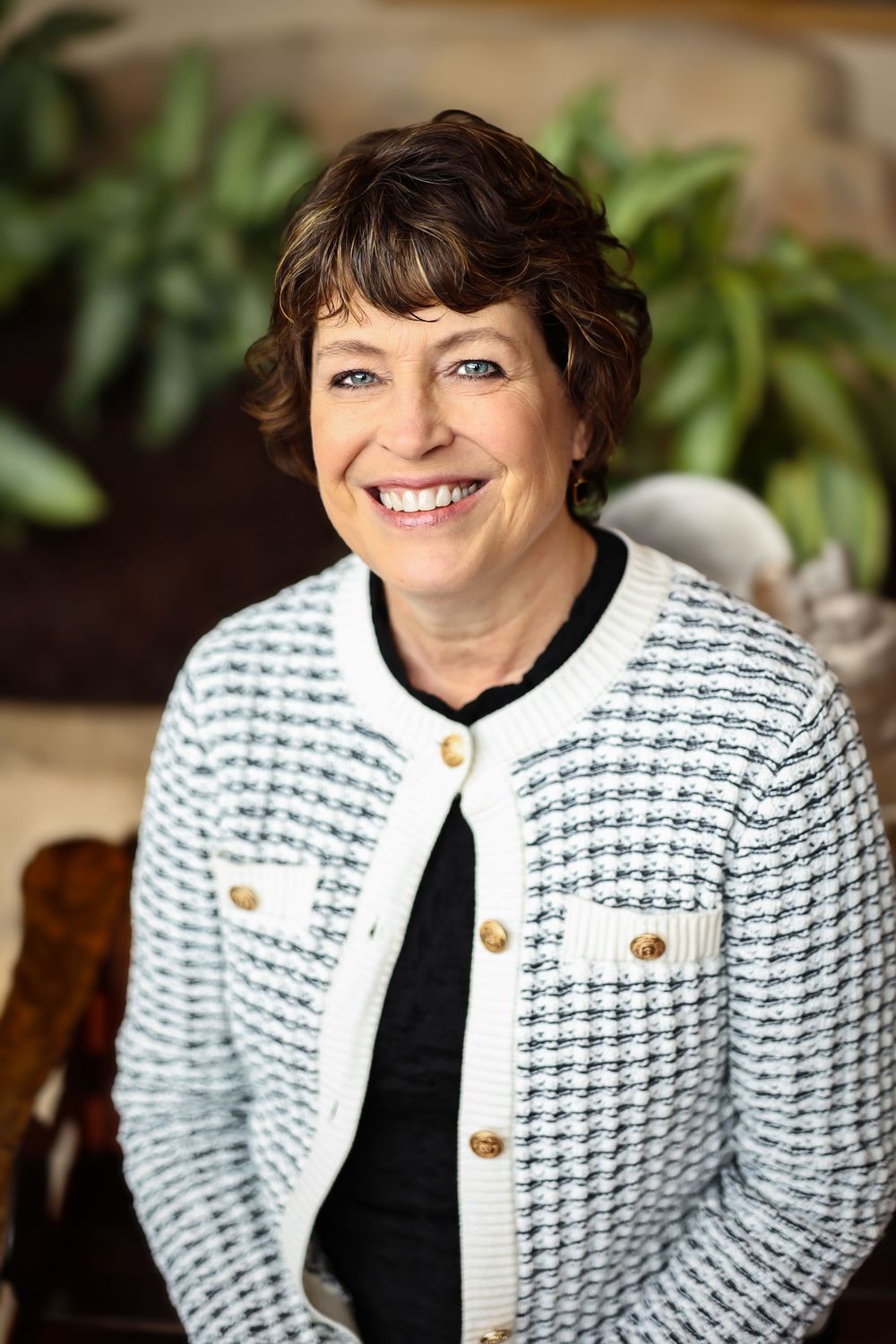 Professional headshots wearing textured white jacket with gold buttons against natural background.