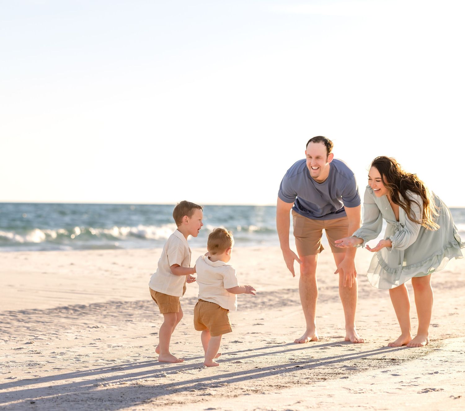Family in casual beige clothing walking together on a sandy beach at sunset creating a warm and relaxing scene.