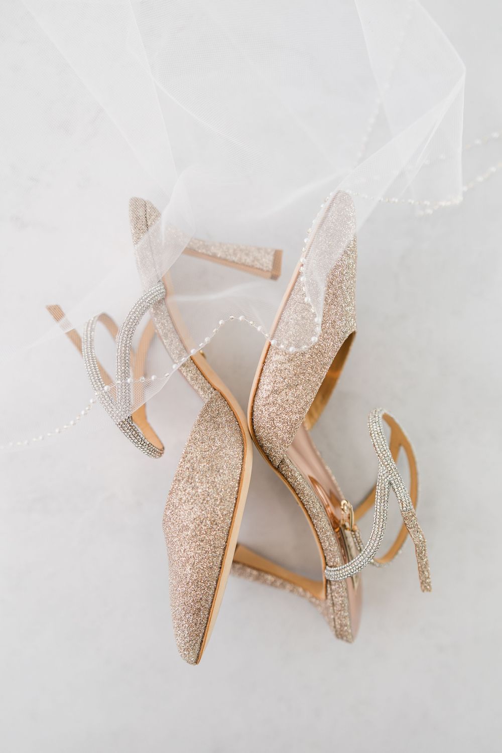 Sparkly champagne-colored slingback heels with glitter detail arranged on white fabric background.