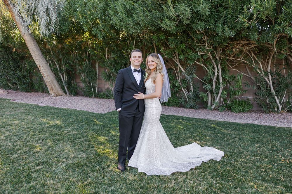 A couple in wedding attire embraces while standing in a lush garden setting during their outdoor celebration.