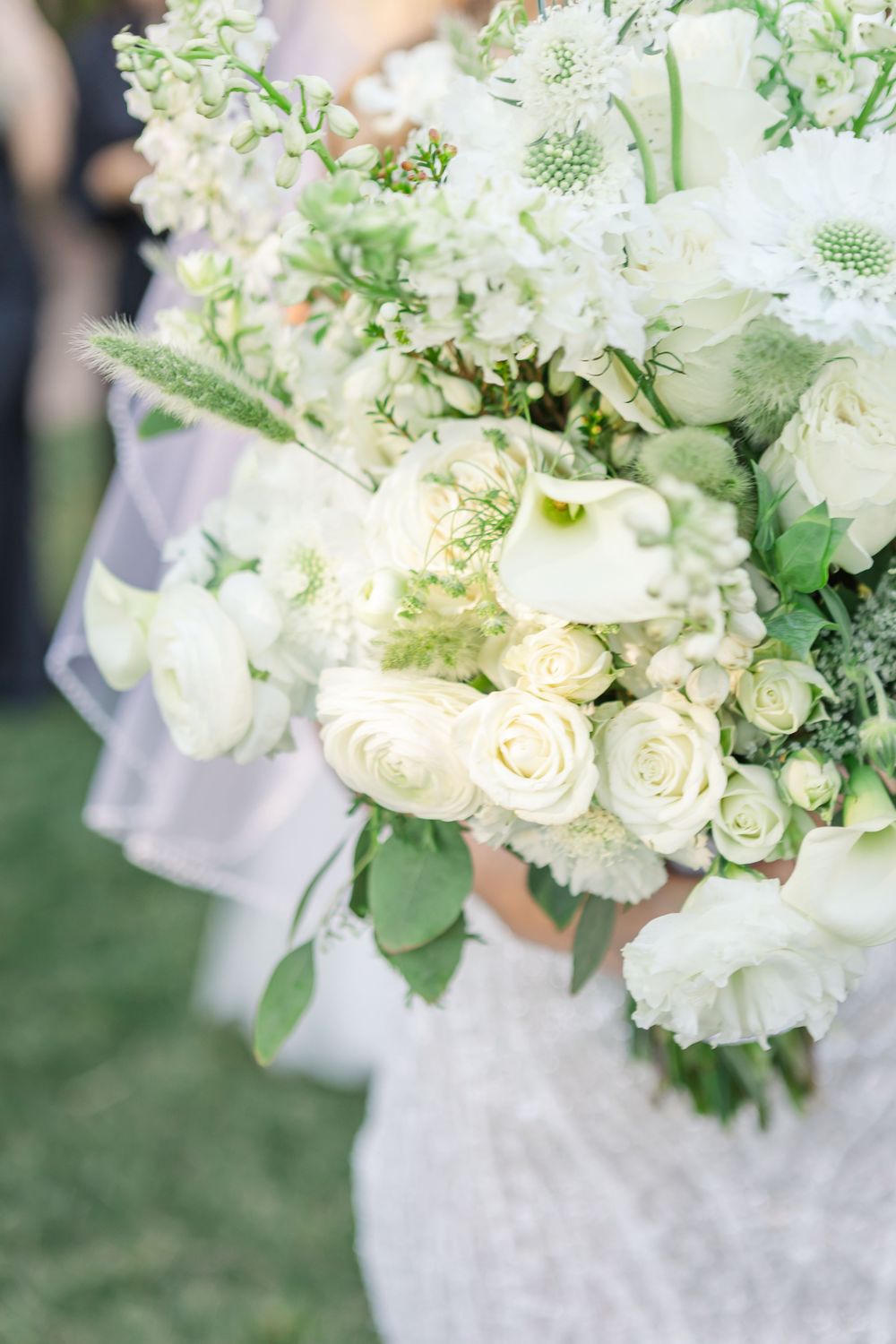 Close-up view of an elegant white wedding bouquet with roses, carnations and delicate greenery against a soft blurred background.