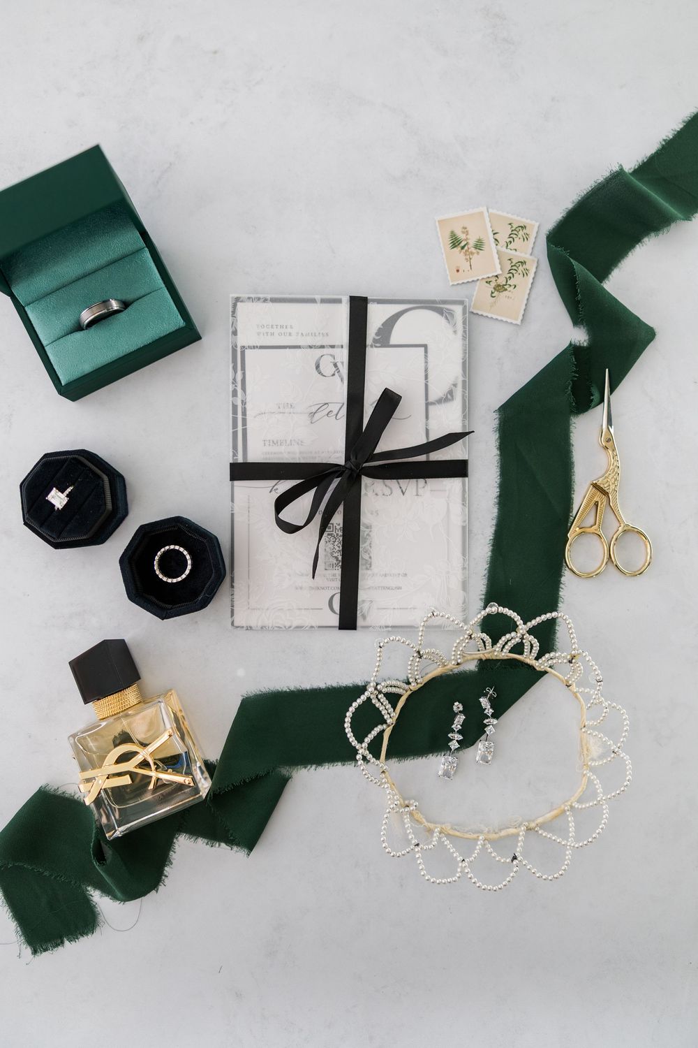 Elegant wedding accessories in green and white with gold jewelry and ribbons arranged on a light gray background.