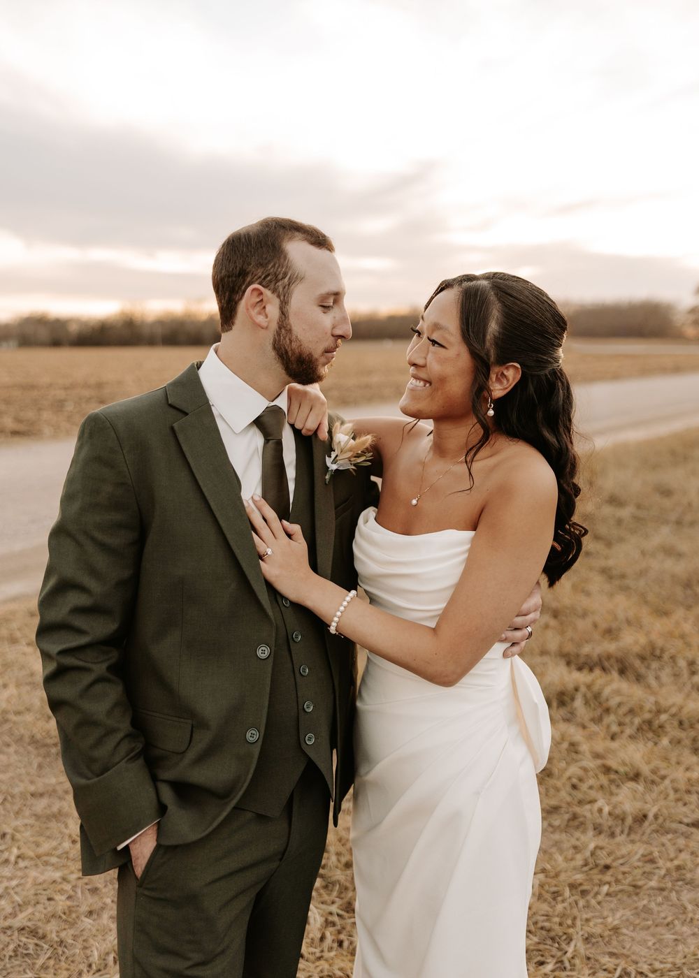 A romantic sunset portrait of newlyweds embracing in an outdoor field with warm lighting.
