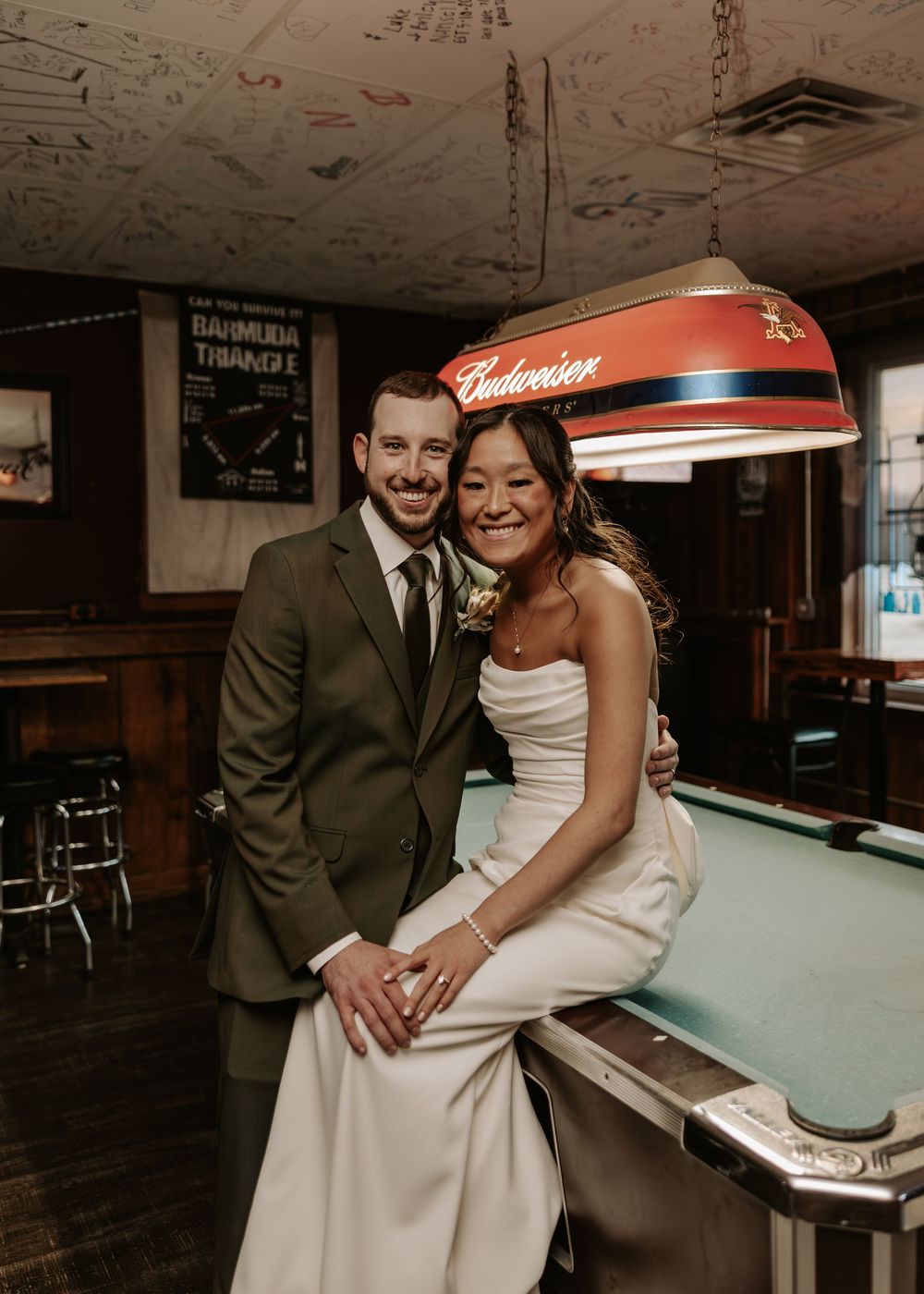 Newlyweds share playful moments around a pool table in a dimly lit bar.