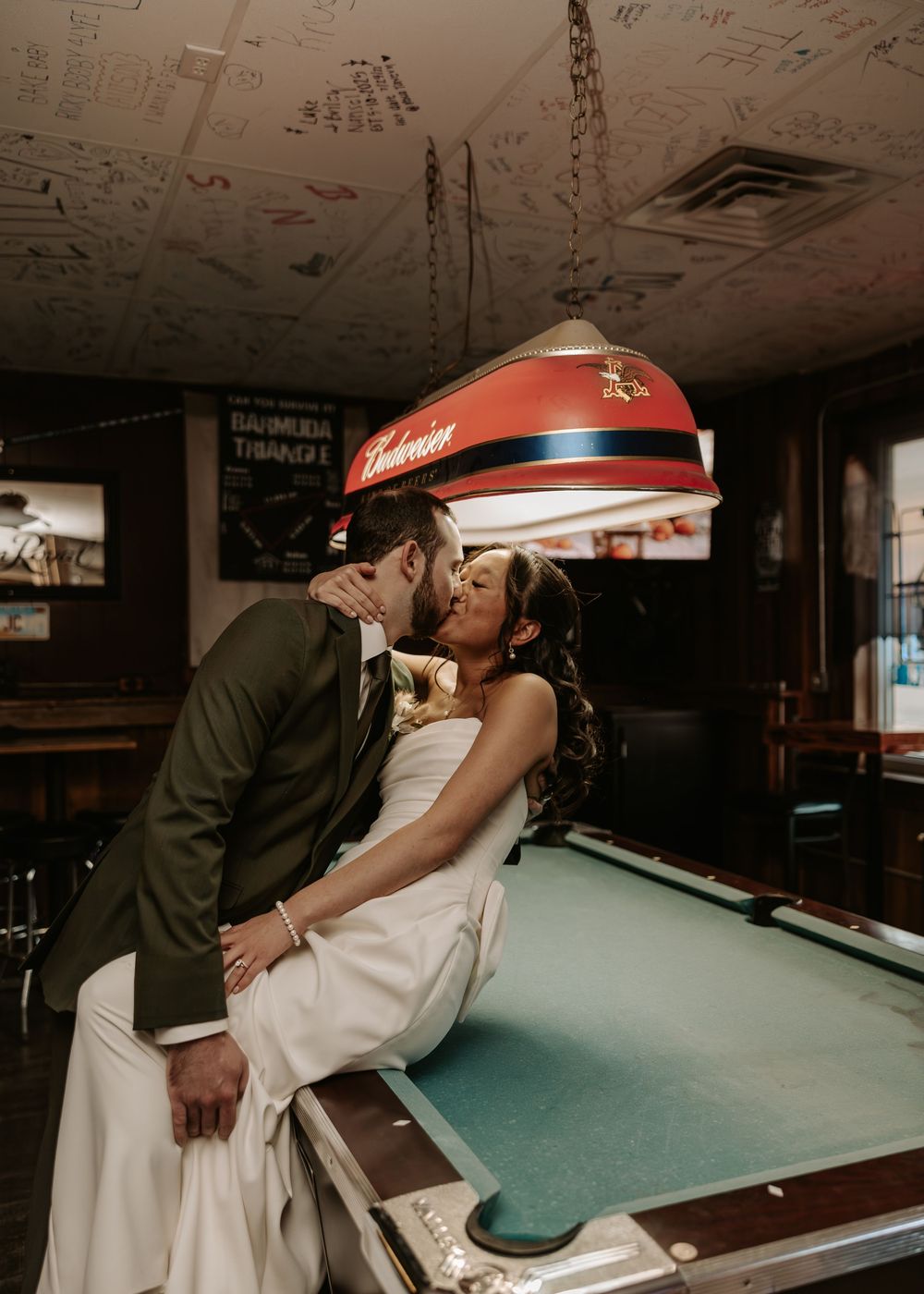 A couple shares a romantic moment near a pool table in a dimly lit room.