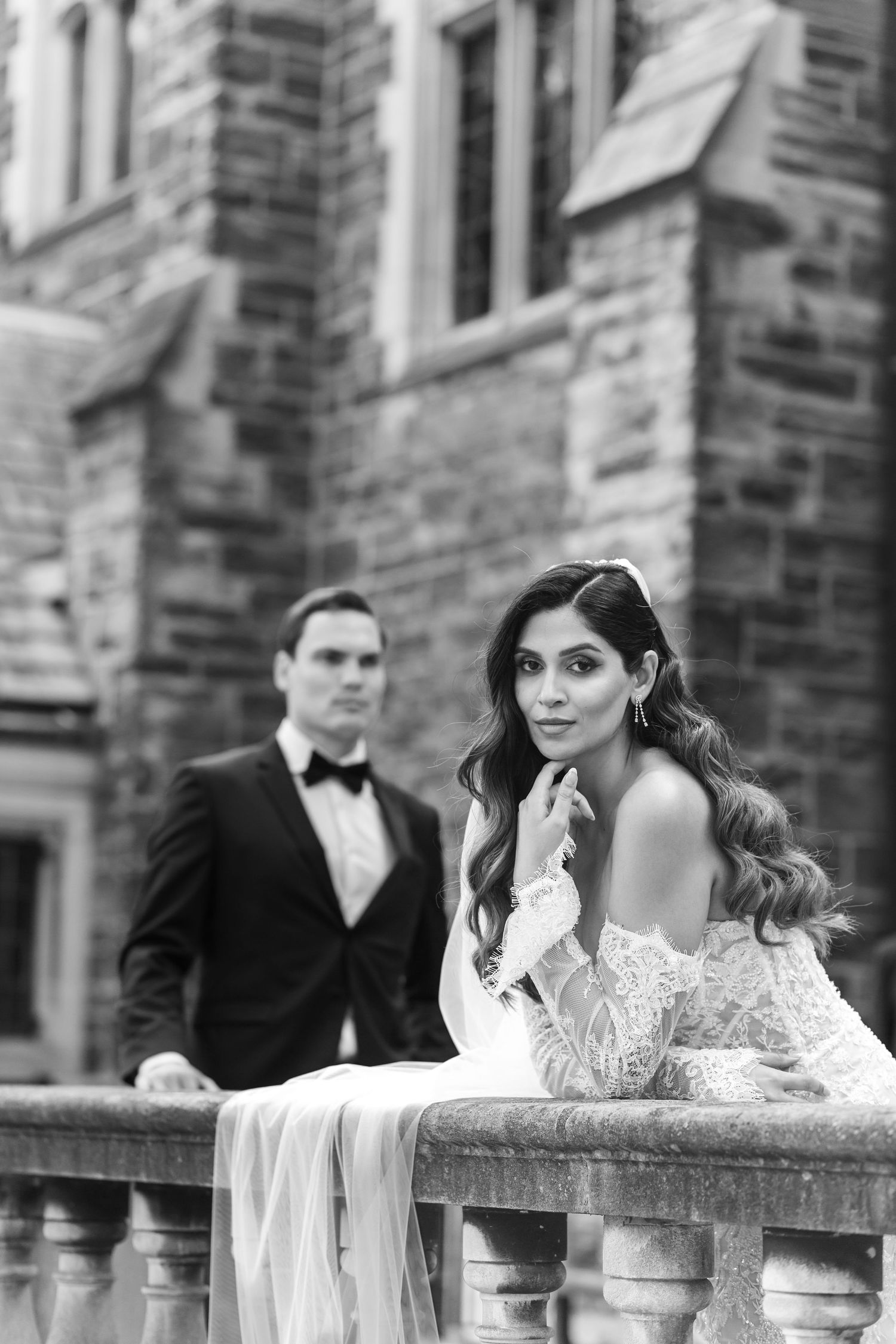 Black and white wedding photo of a couple posing by stone balustrade at elegant historic building.