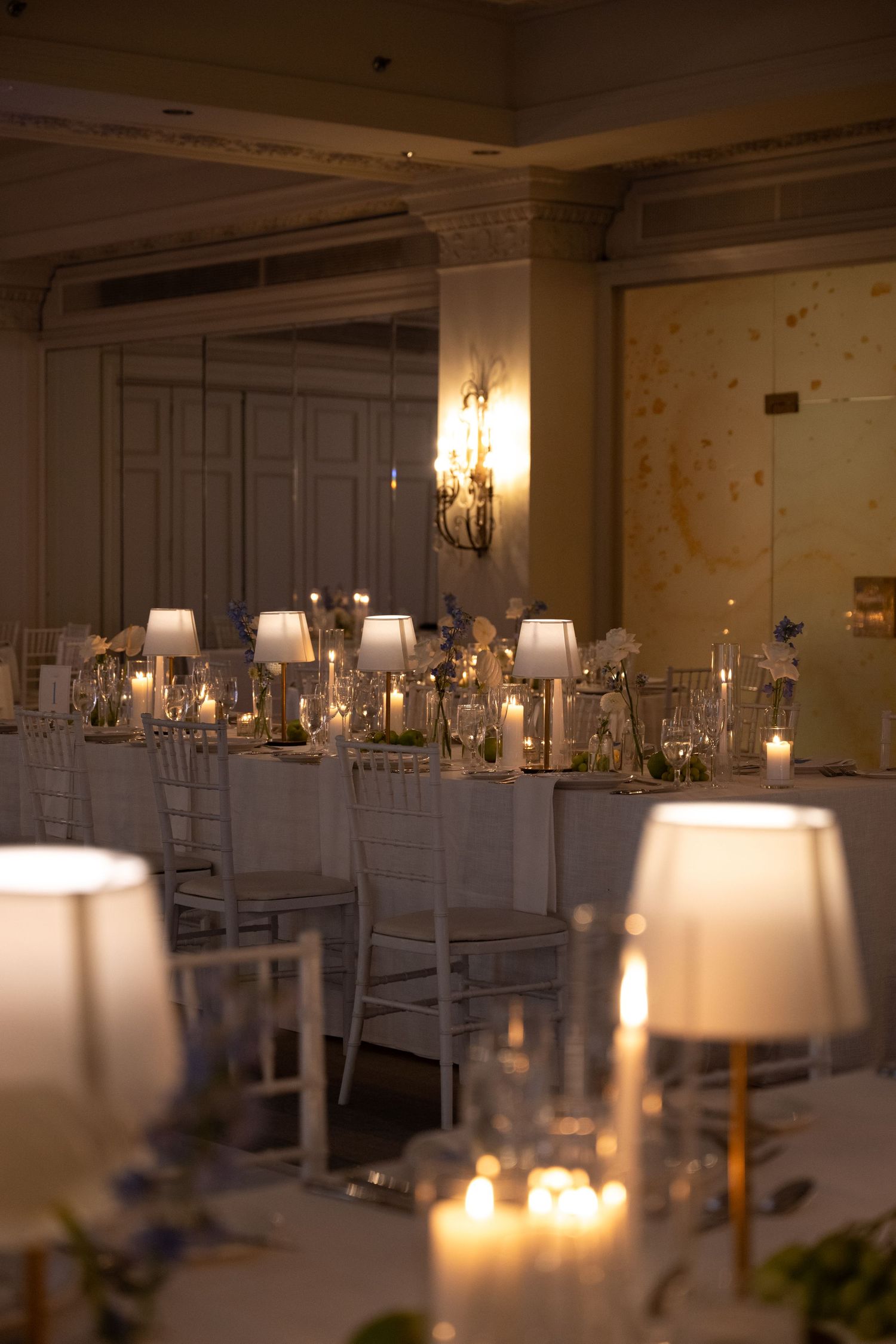 Elegant candlelit wedding reception hall with white chairs, small table lamps, and glowing candles creating a warm ambiance.