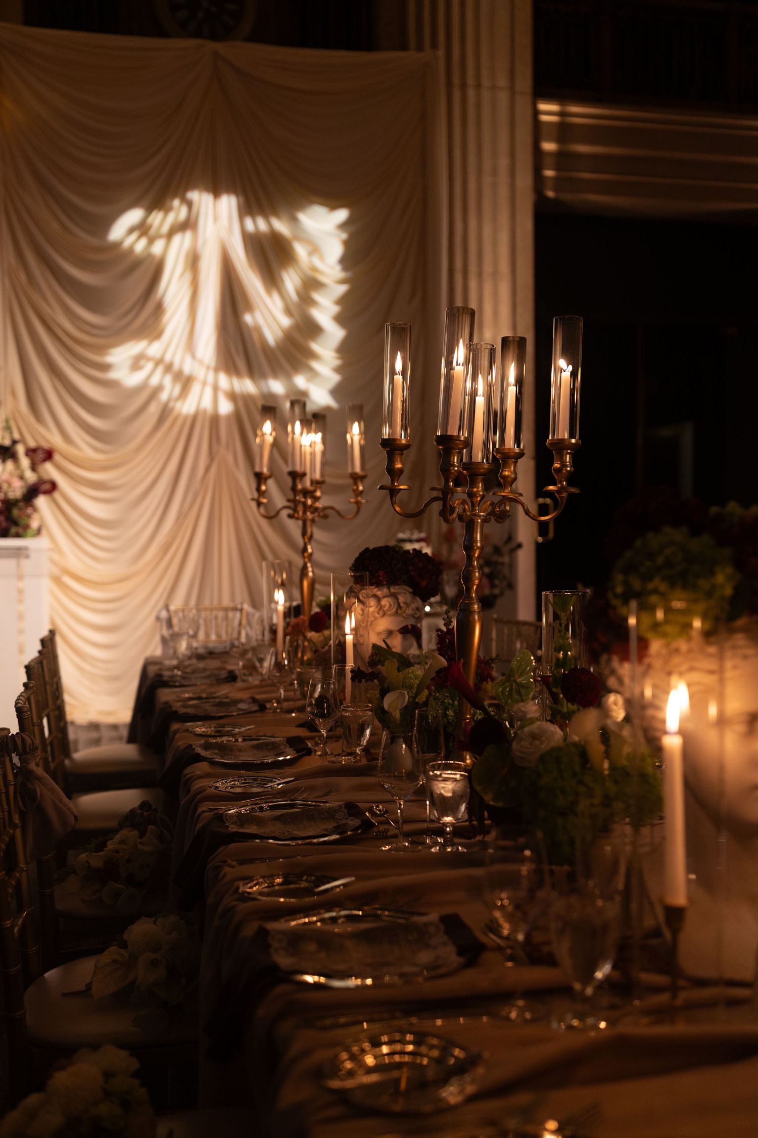 Elegant wedding reception table with gold candelabras, floral centerpieces, and candlelight in a draped ballroom.
