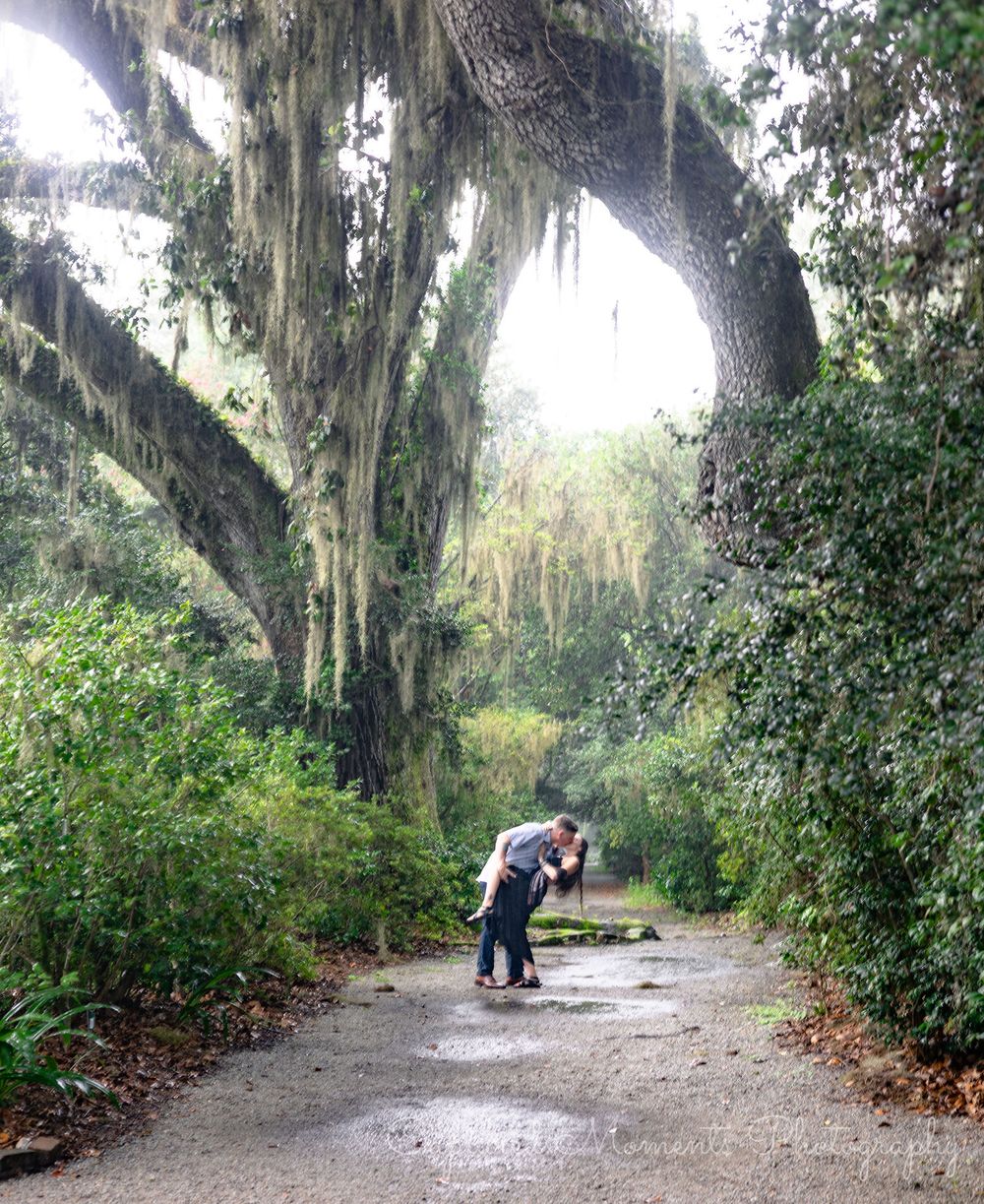 Romantic couple shares tender moments along a scenic Spanish moss-draped pathway in a Southern garden setting.