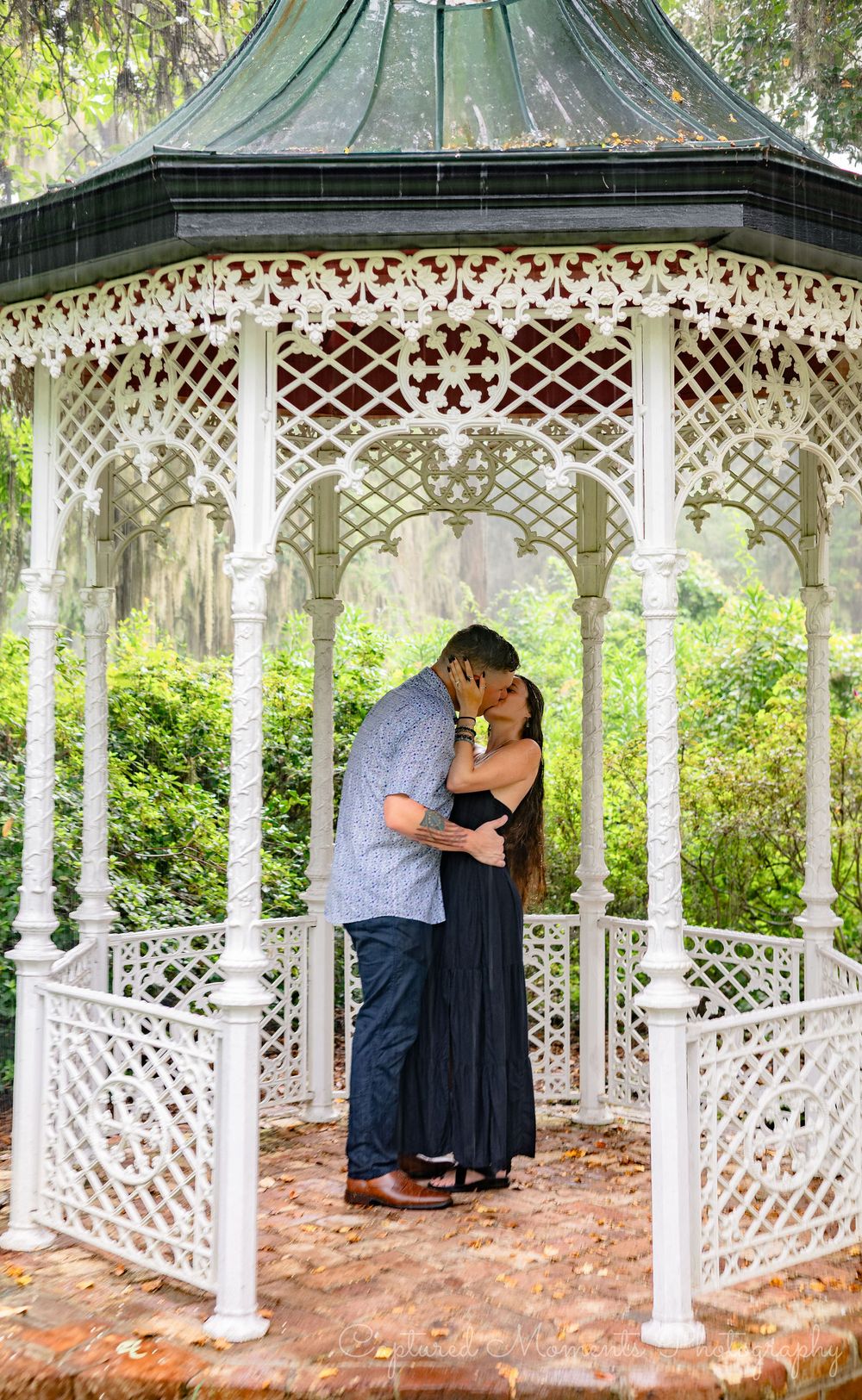 A romantic moment captured in a white Victorian-style gazebo surrounded by lush greenery in a garden setting.