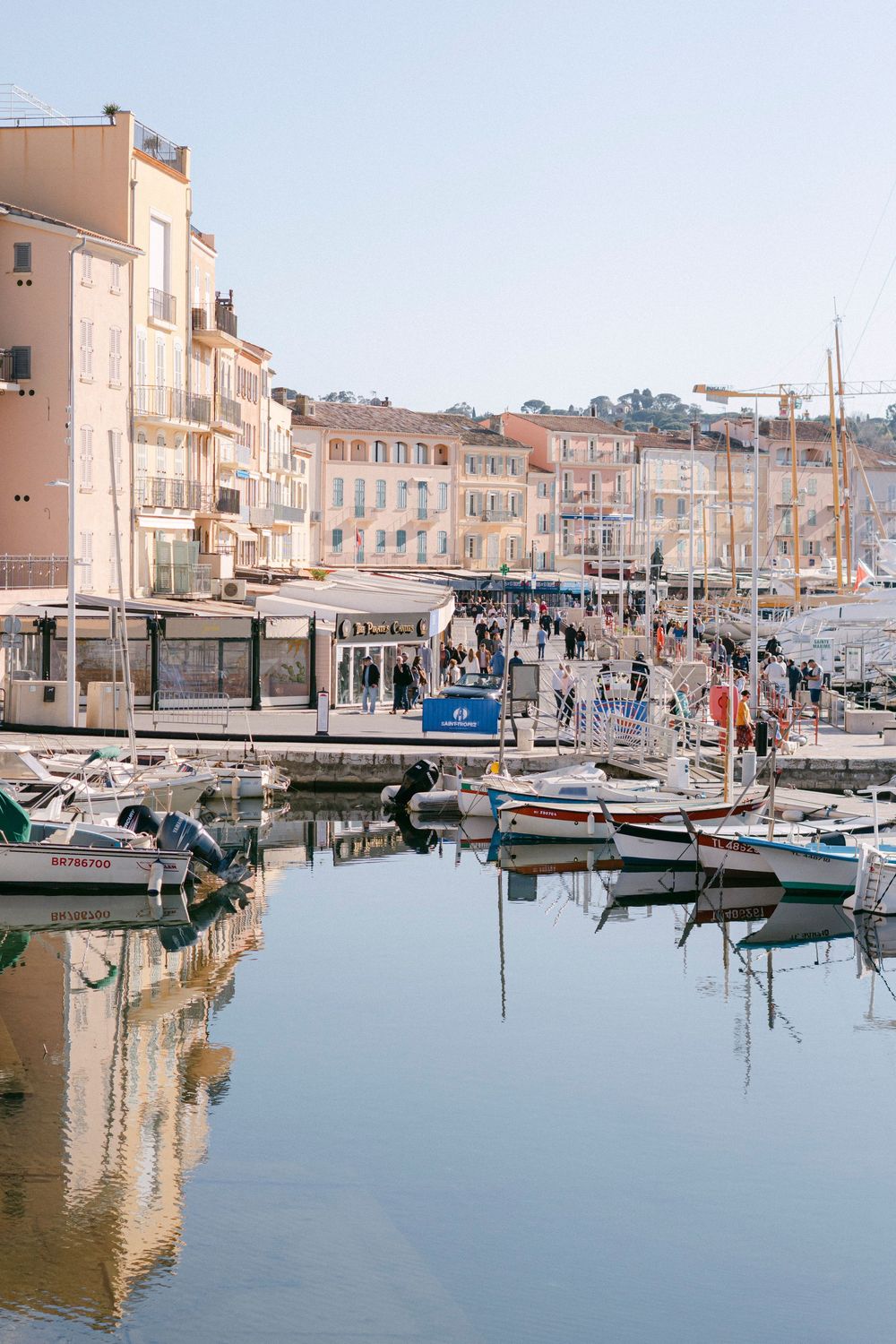 Boats docked in a picturesque Mediterranean harbor with pastel buildings and waterfront cafes in Saint-Tropez, France.