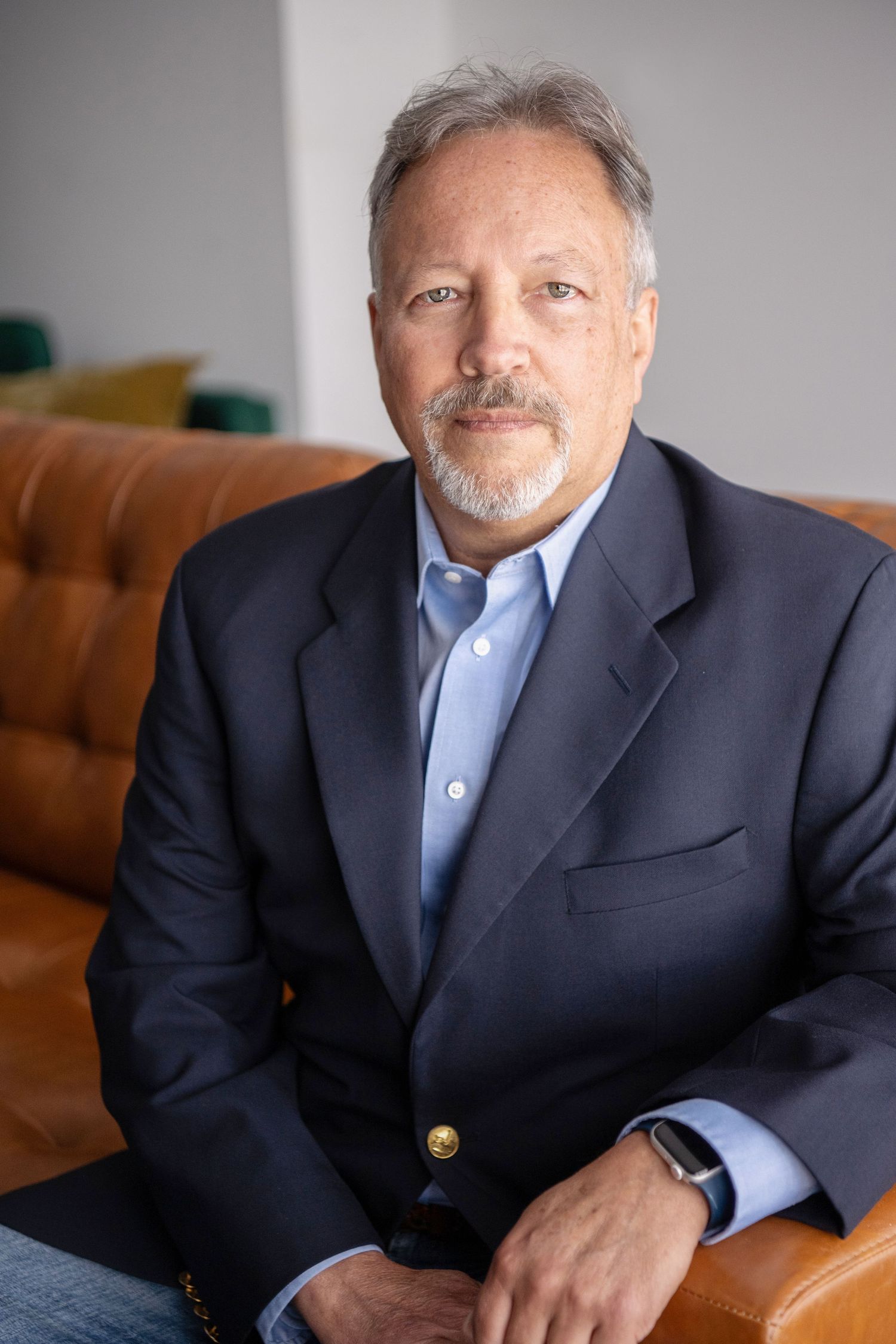 Professional portrait series showing a man in a navy suit jacket and blue shirt seated against a light background.