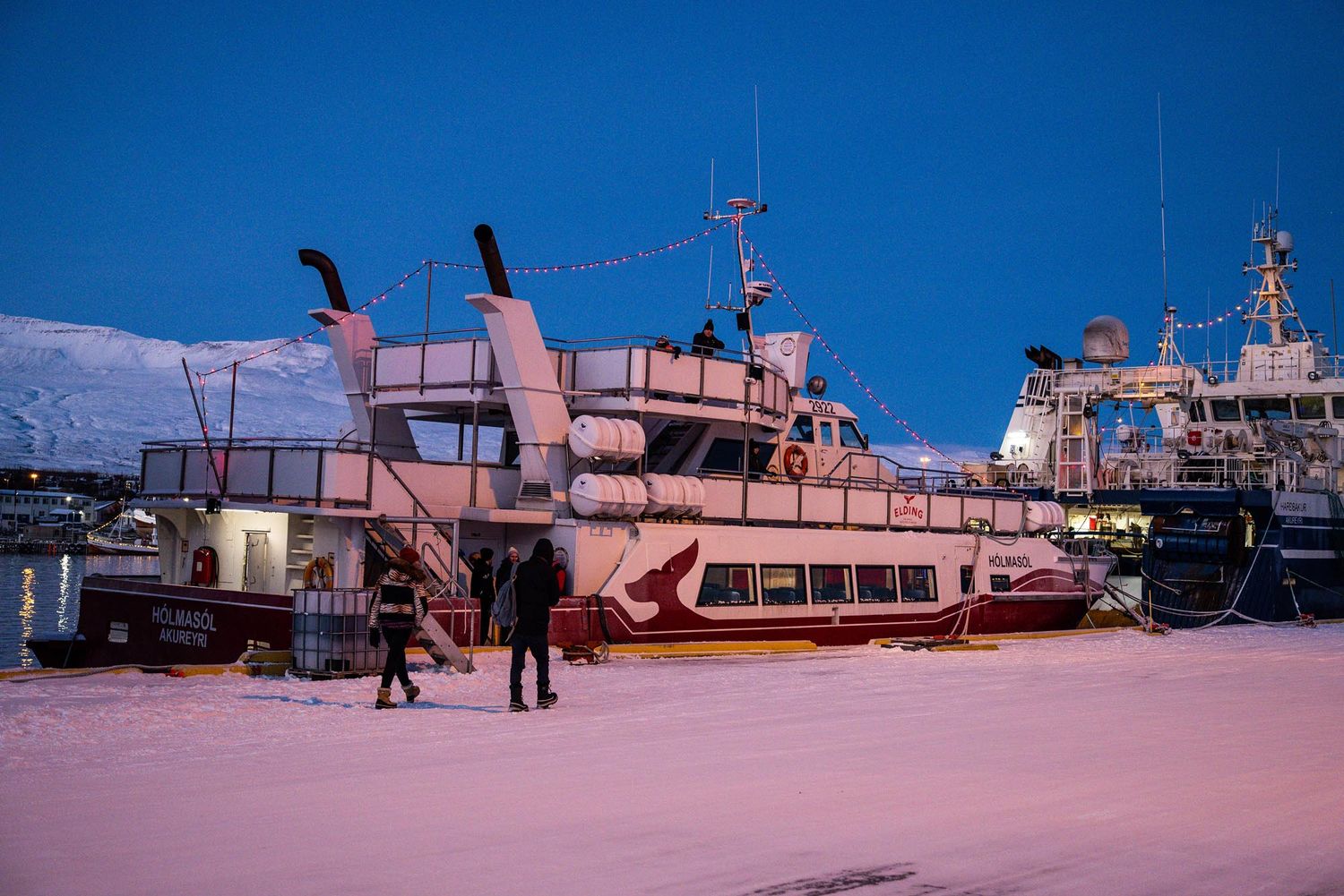 Fishing boats docked at a harbor during sunset with pink and blue hues in the sky.