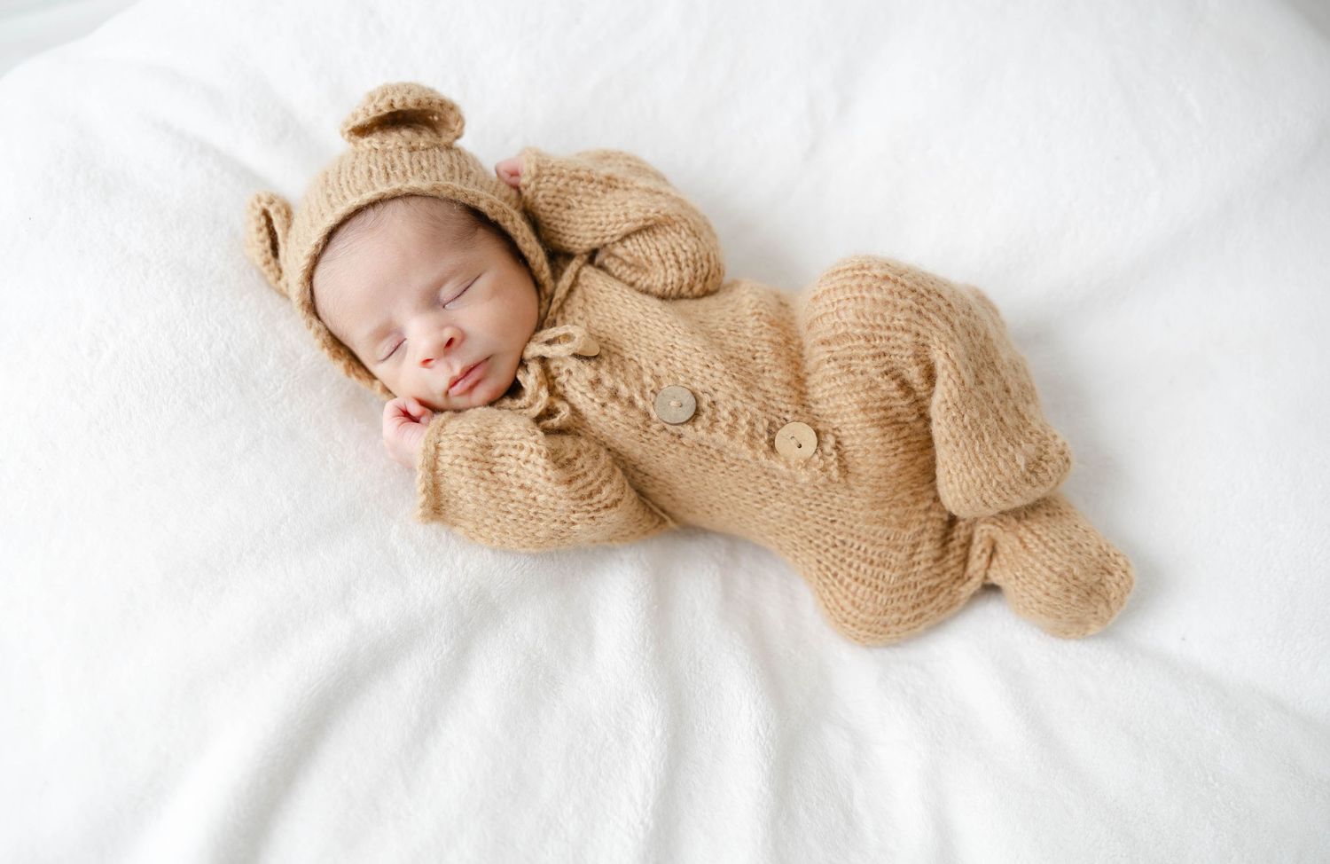 Sleeping newborn baby wearing a knit bonnet and wrapped in a neutral blanket during a lifestyle newborn session.