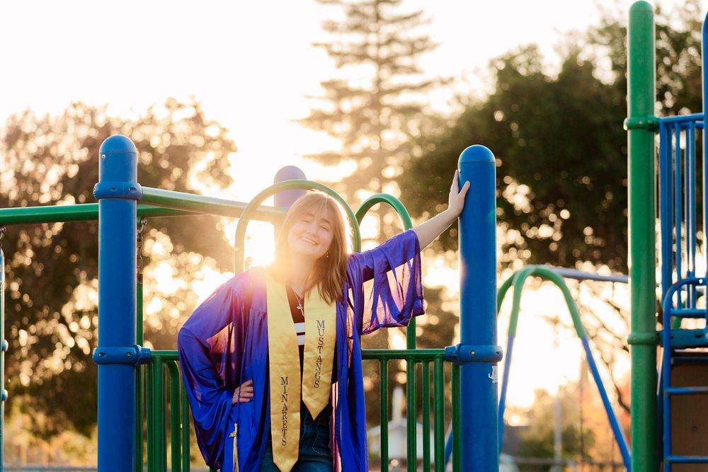 Colorful playground equipment silhouetted against a golden sunset with sun flare peeking through the metal bars.