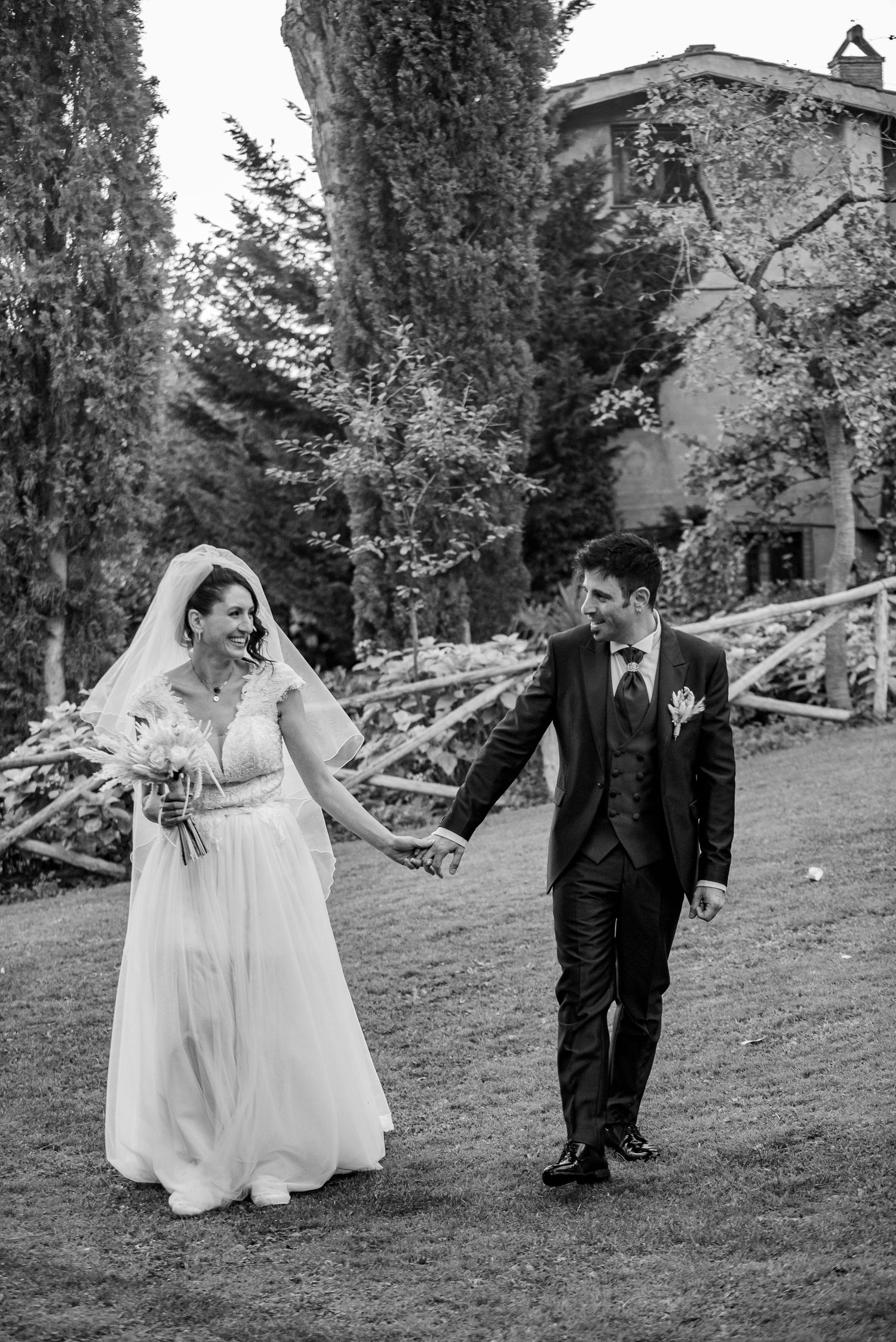 A bride and groom playfully run and chase each other on a grassy hillside in a series of black and white wedding photos.