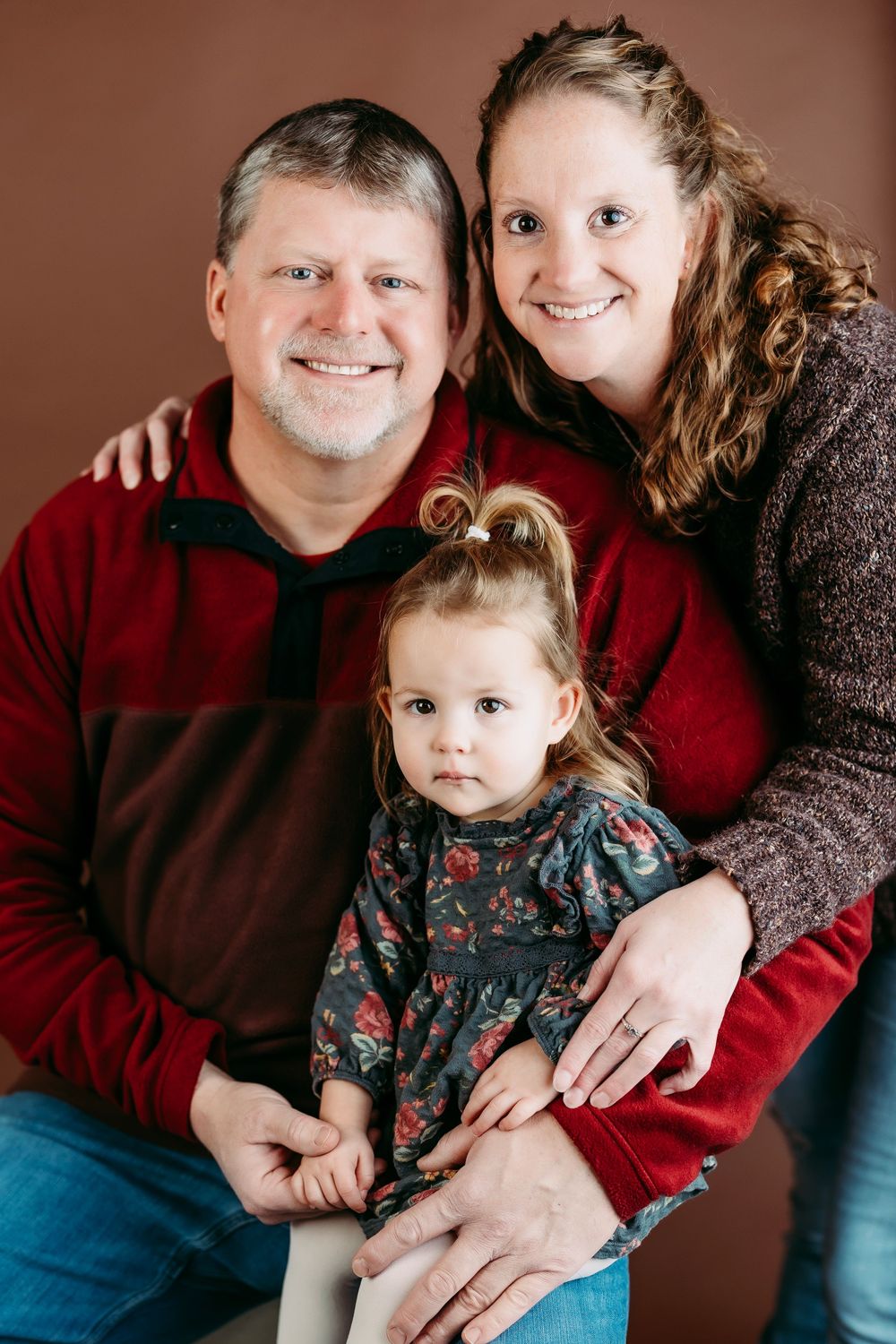 A family portrait series showing tender moments between parents and child against a dark brown backdrop.