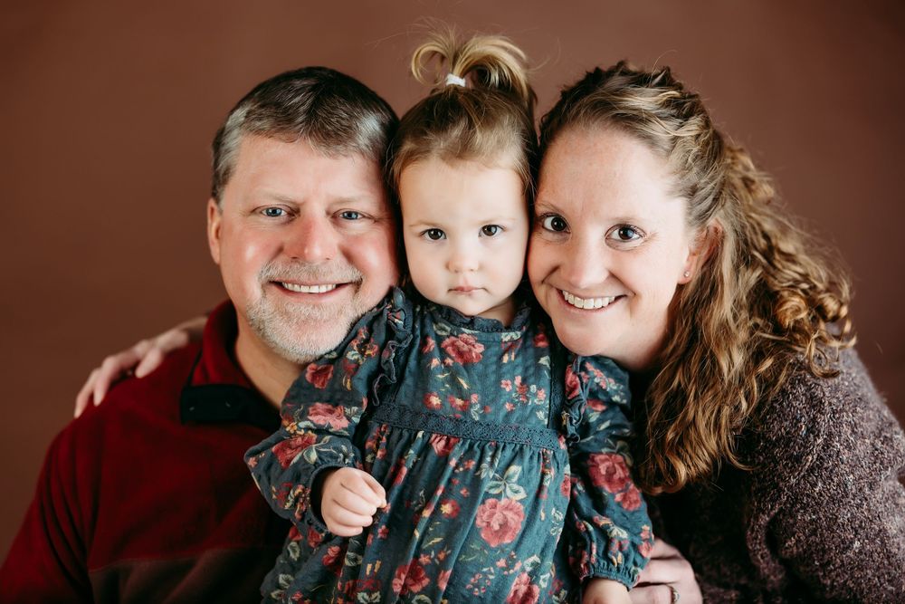 A family poses together in coordinated burgundy and teal outfits against a dark background for professional portraits.