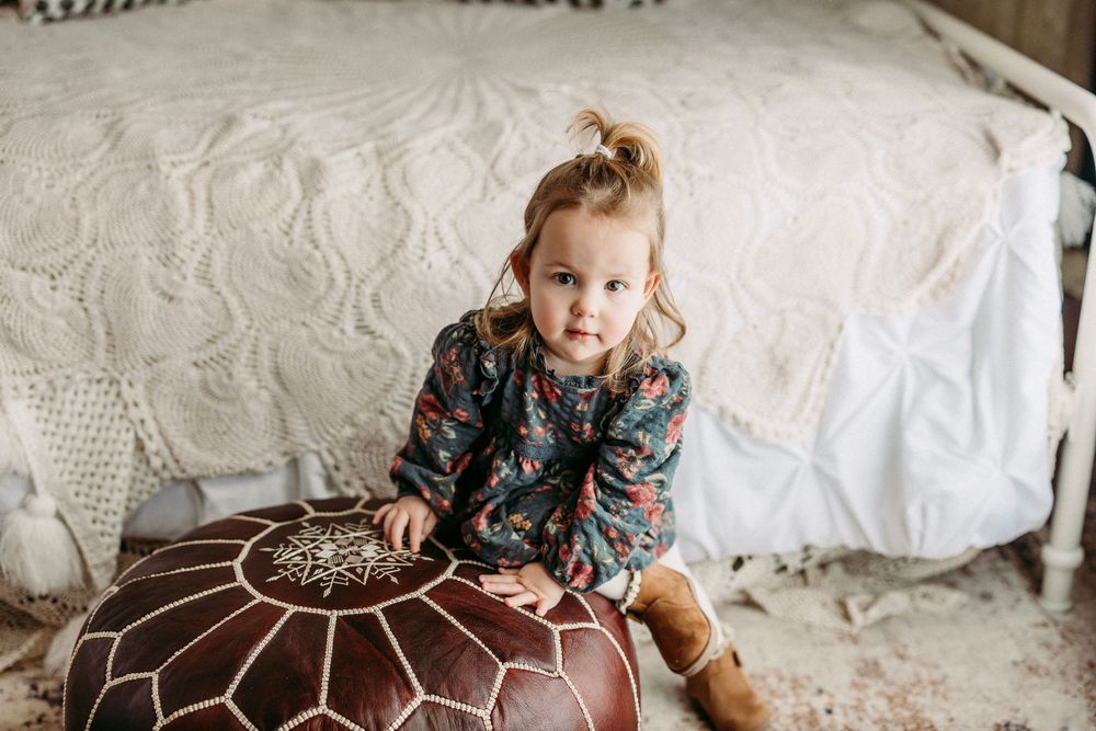 A child sits on a cozy white bed wearing a floral dress while playing with a toy.