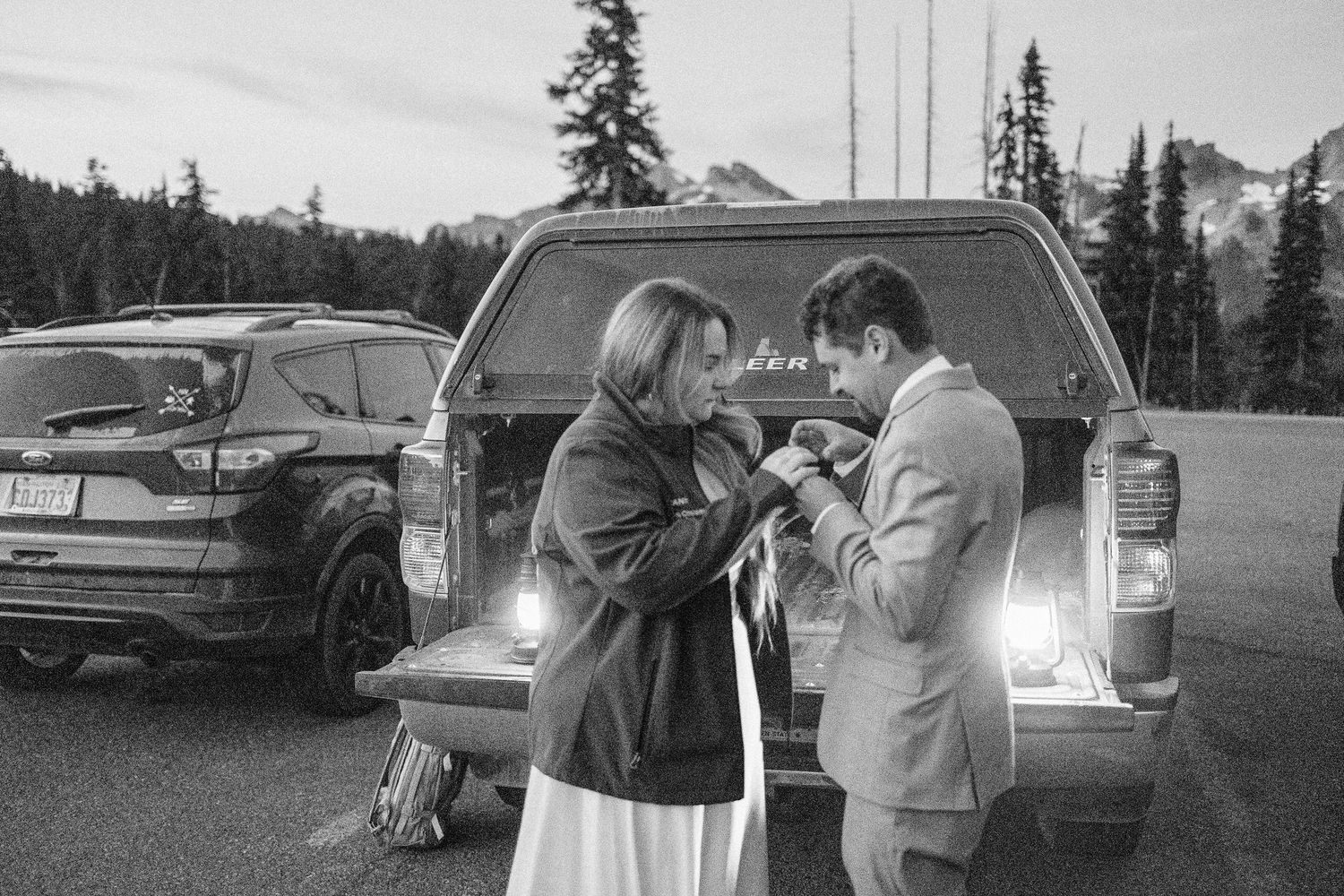 black and white photo showing wedding couple getting ready by cars and mountains in a scenic outdoor setting.