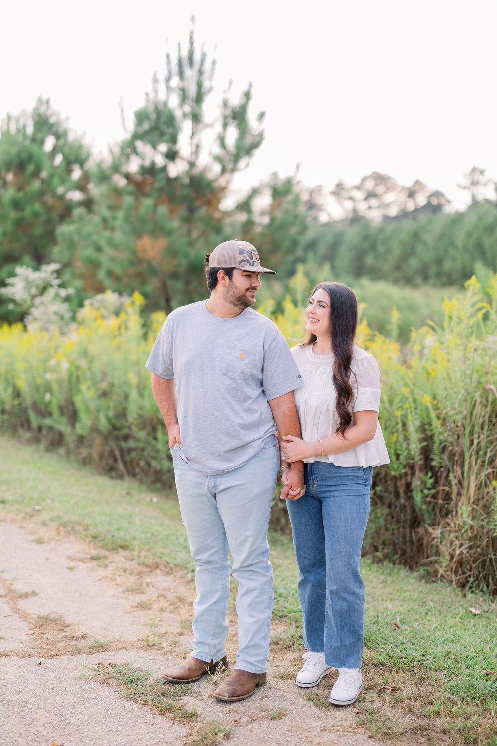Couple walking together on a dirt path surrounded by wildflowers and greenery in a casual outdoor setting.