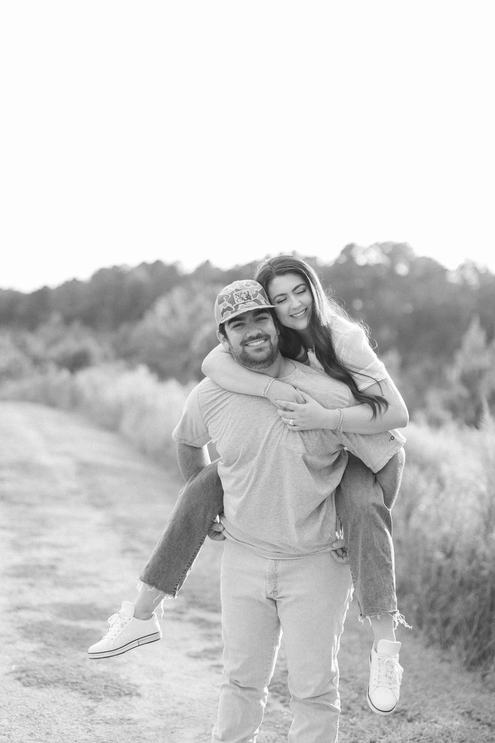 Playful black and white photo of a couple sharing joyful moments on an outdoor path.